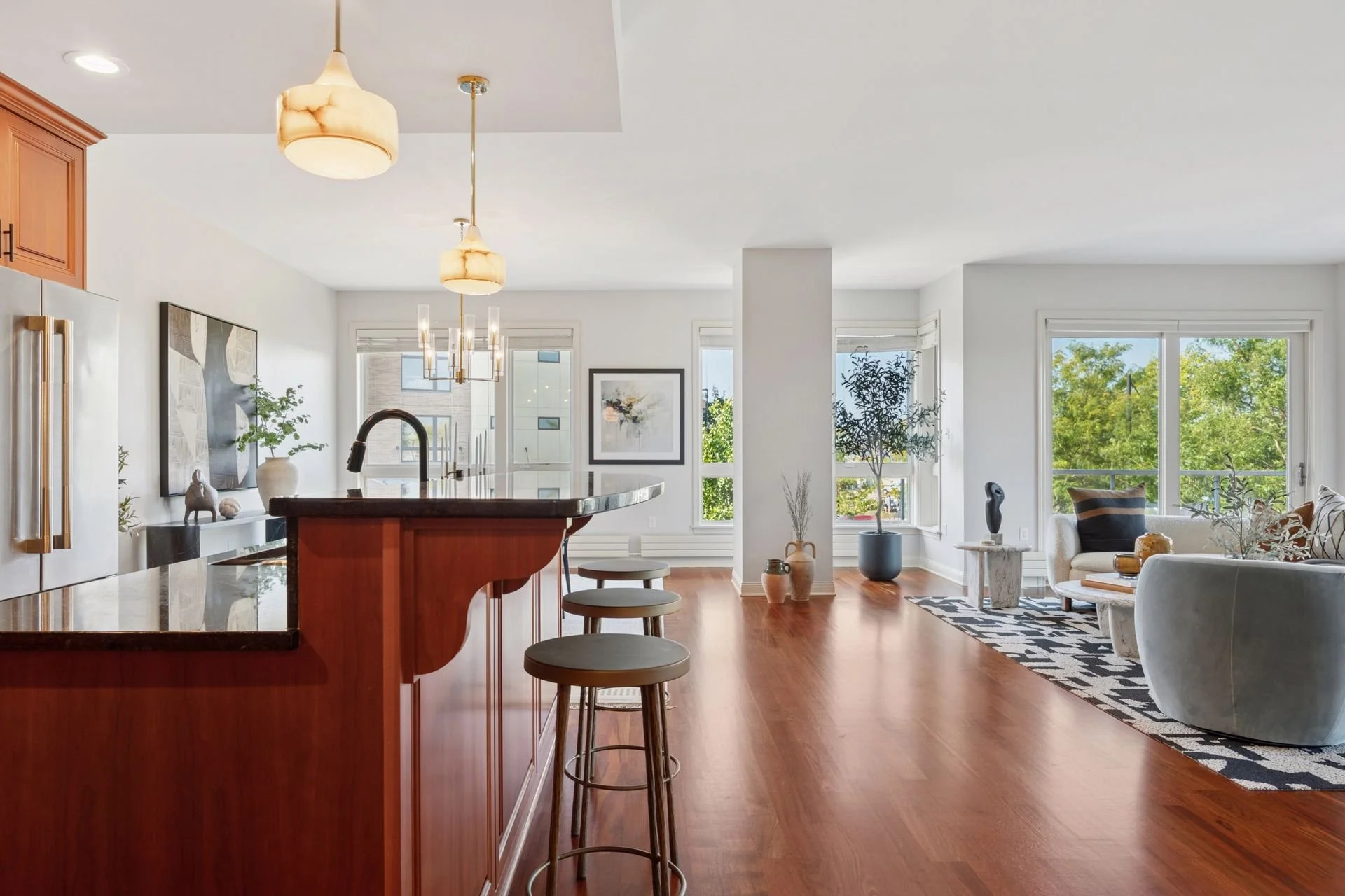 Open-concept living room and kitchen with hardwood floors, white walls, and large windows.