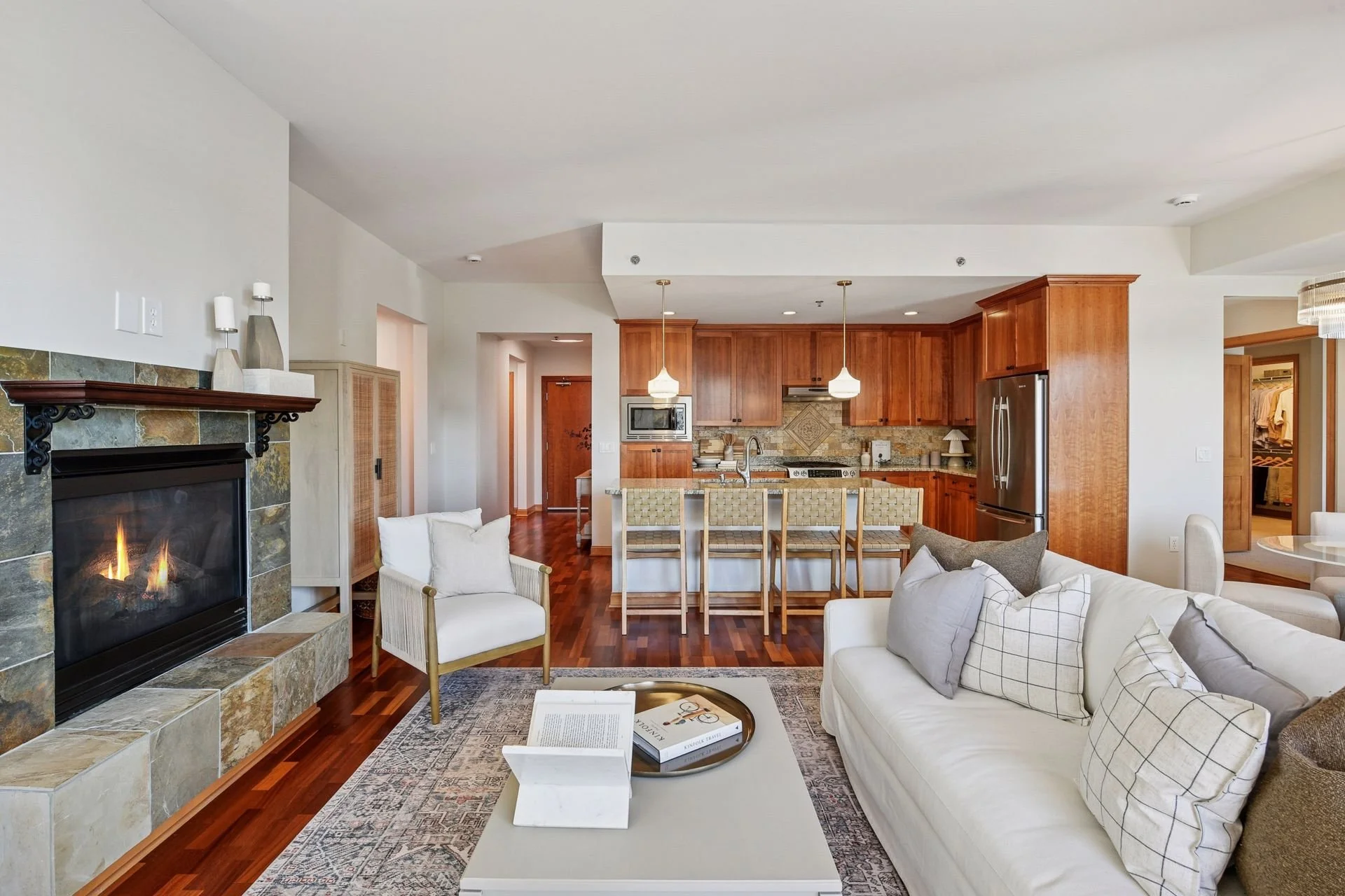 Open-concept living room featuring a fireplace with stone surround, wooden floors, and a kitchen with wooden cabinets, stainless steel appliances, and a spacious island.