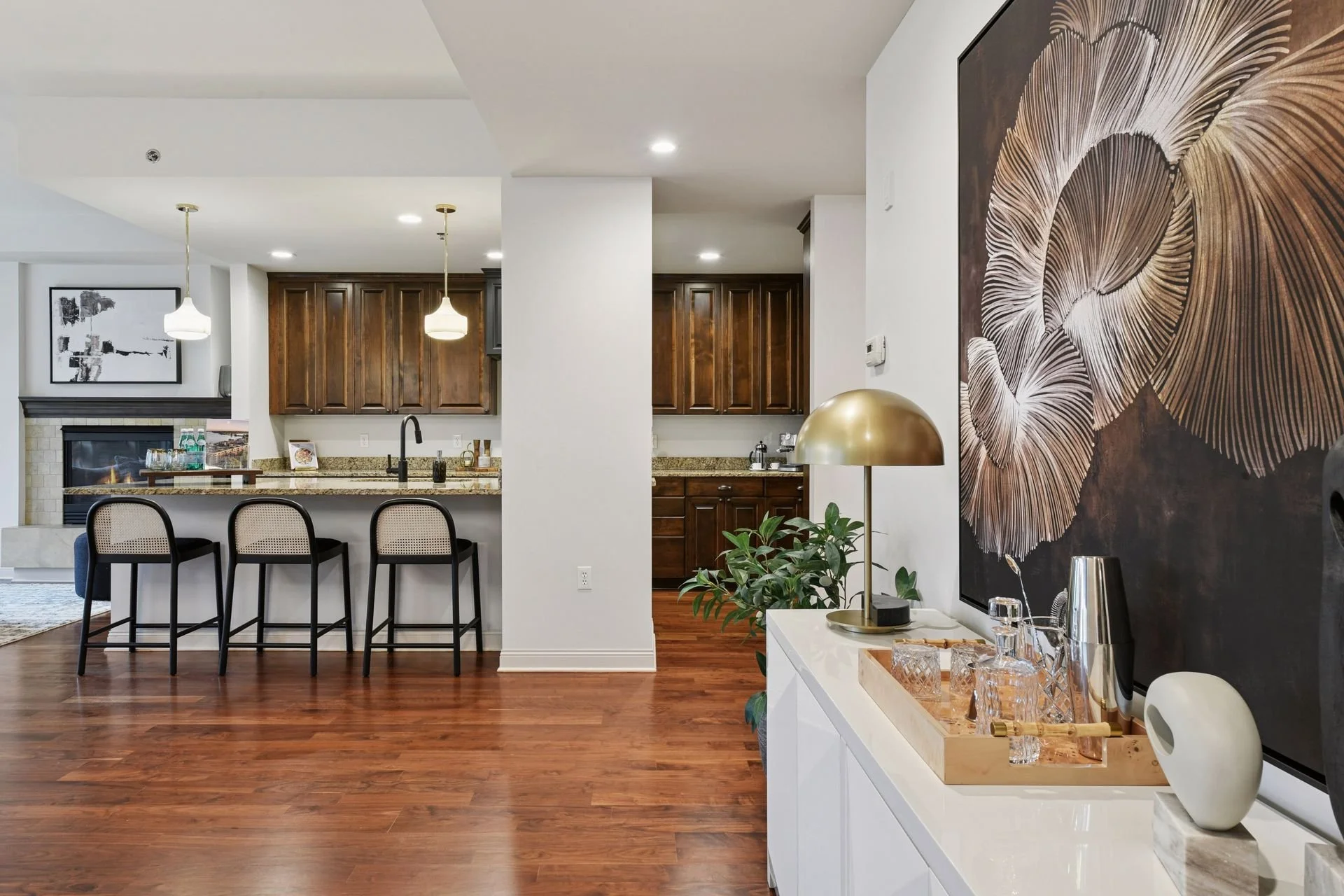 Interior of a modern kitchen and living area with wooden floors, white walls, dark wood cabinets, a spacious island, and a fireplace.