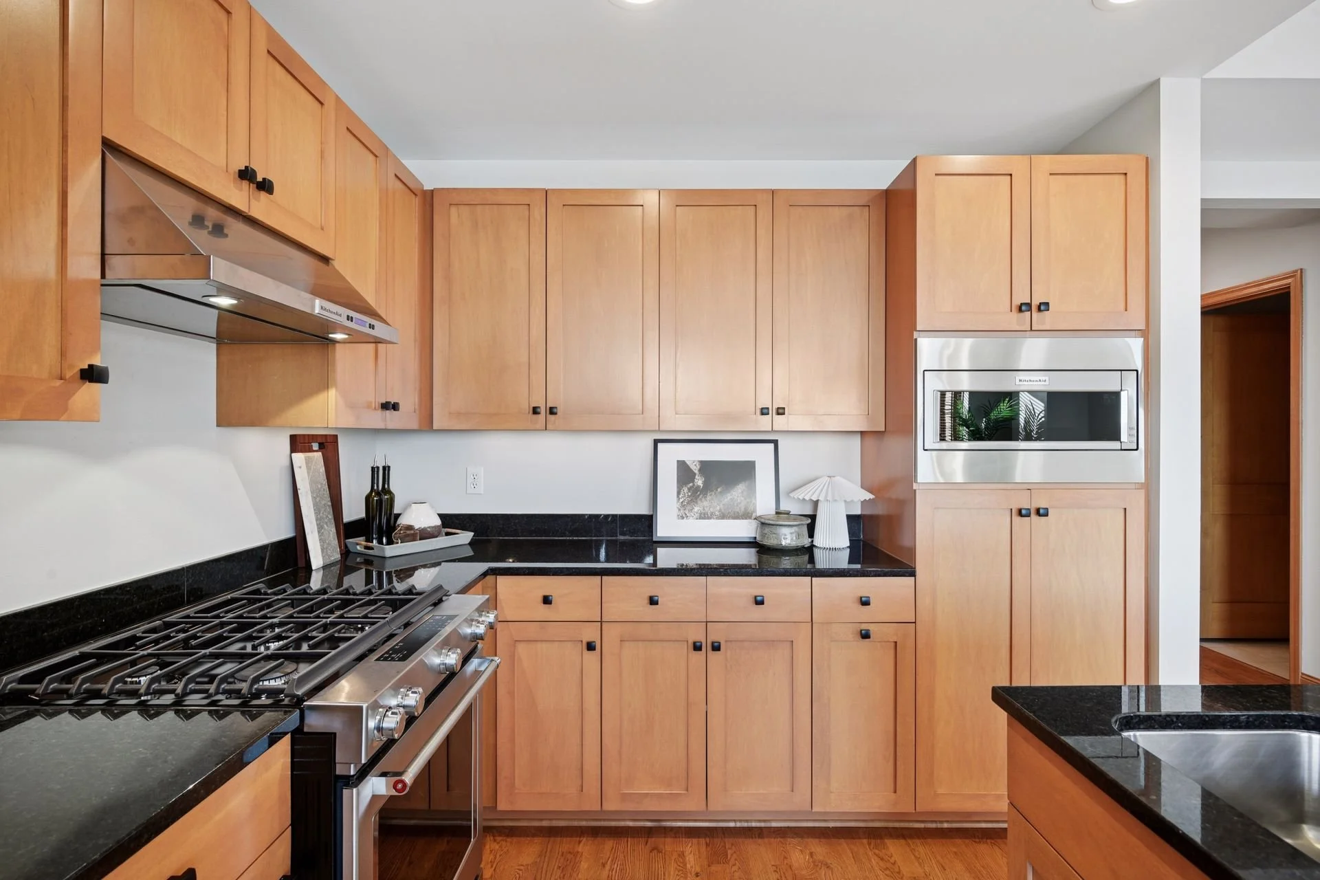 Kitchen with black countertops, wooden cabinets, stainless steel stove, and a microwave.