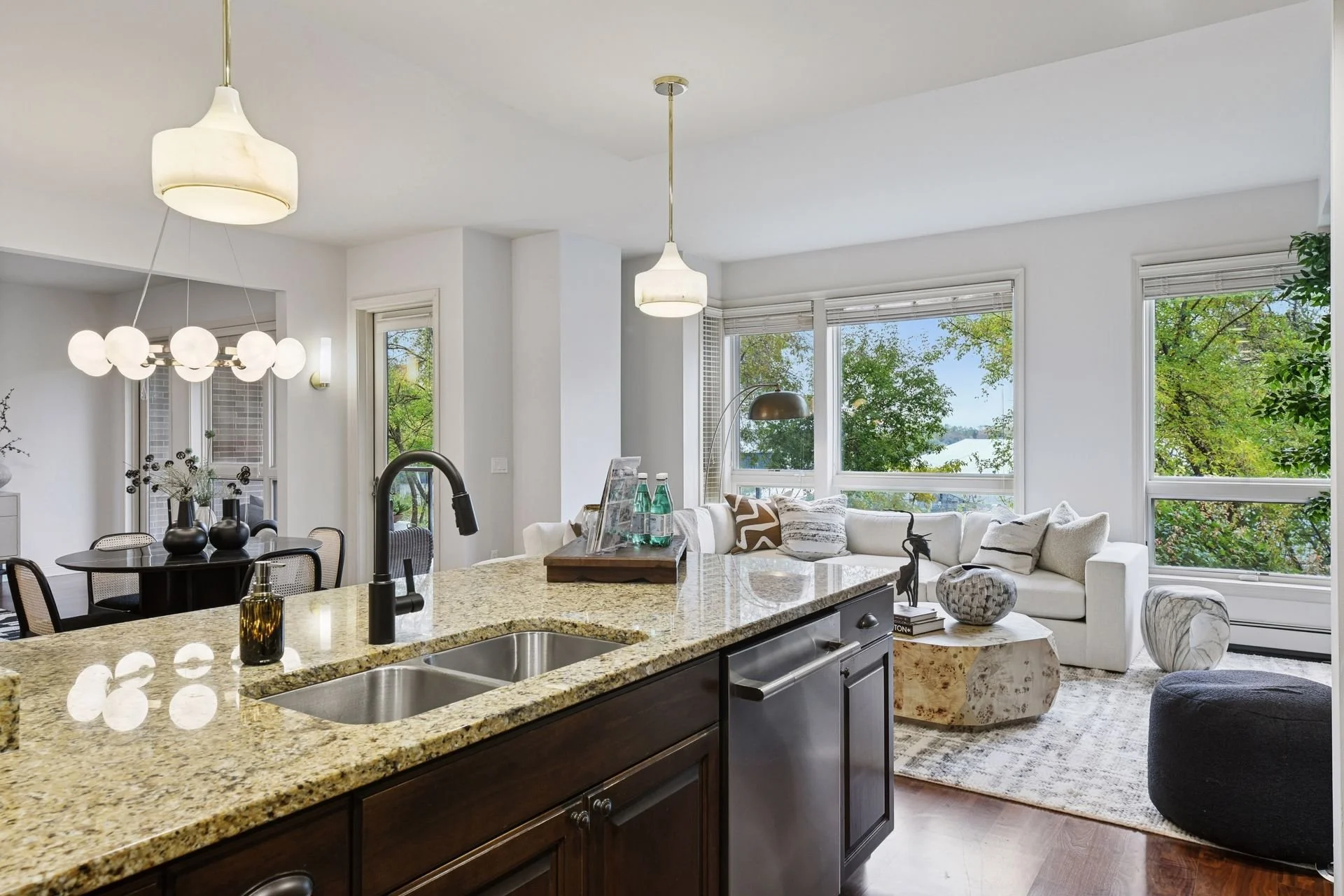 Open-concept living room and kitchen area with large windows showing green outdoor trees.