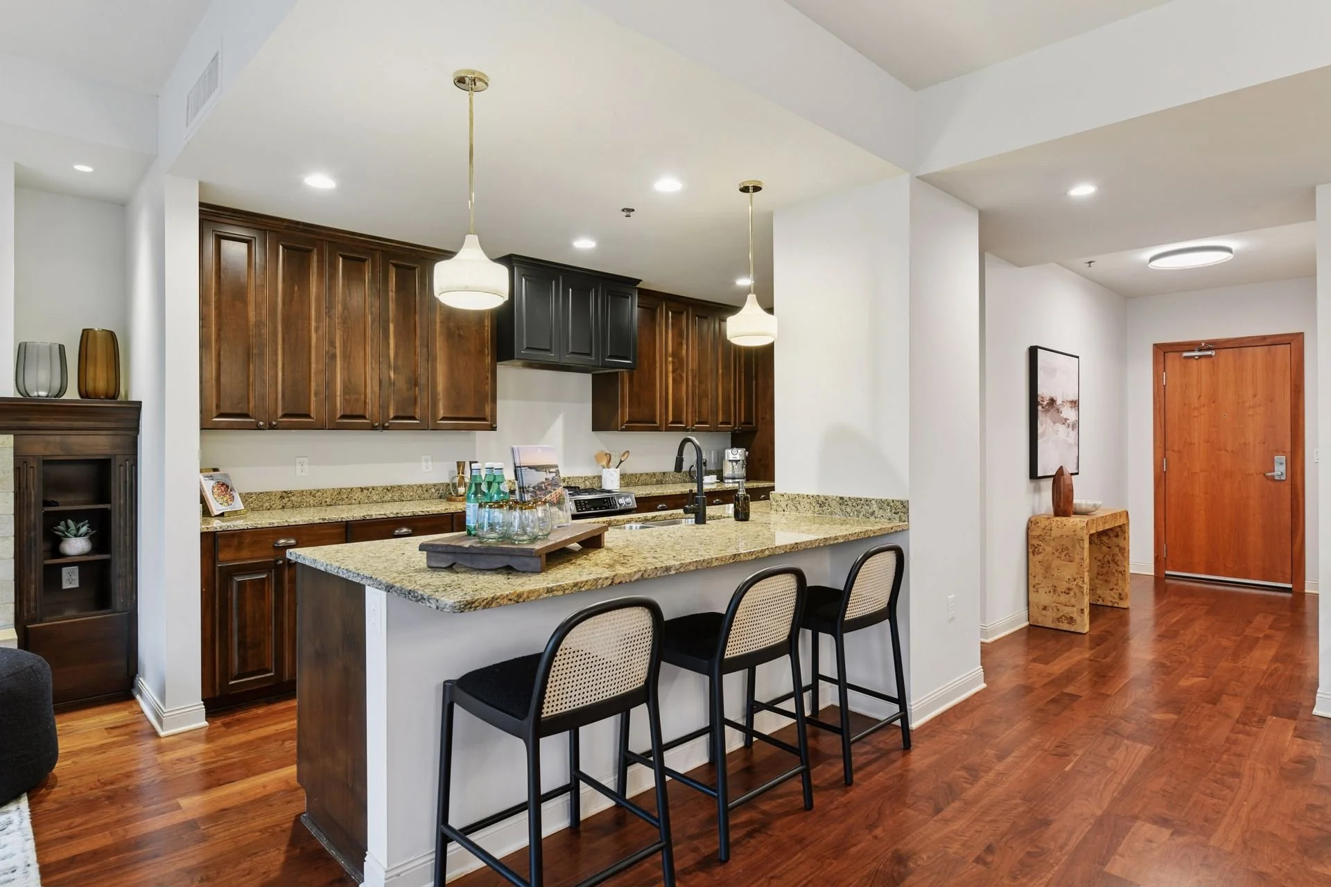 Modern kitchen with wooden cabinets, granite countertops, bar seating, and pendant lighting, in an open floor plan with hardwood floors.