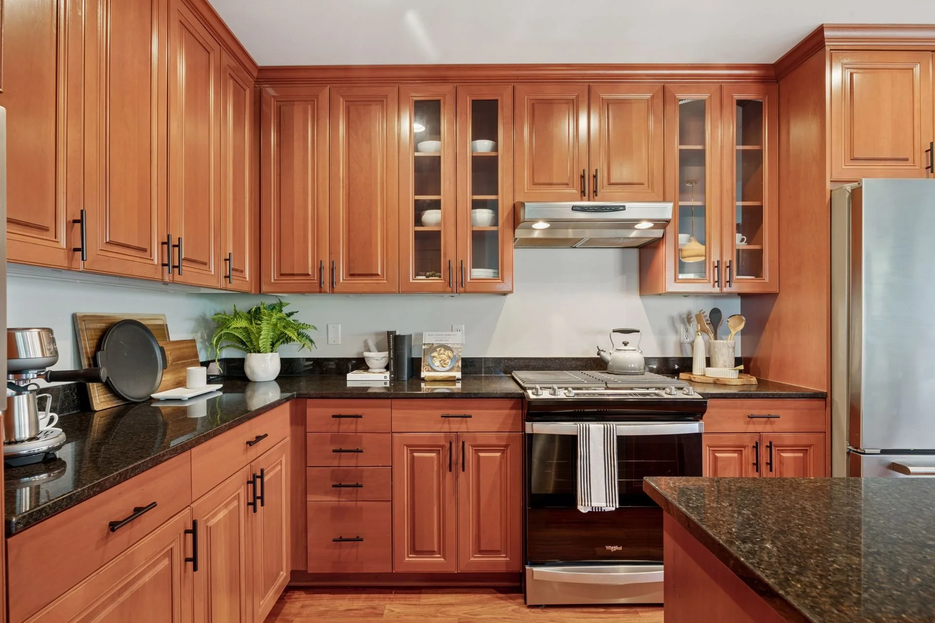 Kitchen with wooden cabinets, black granite countertops, stainless steel stove, and a refrigerator.