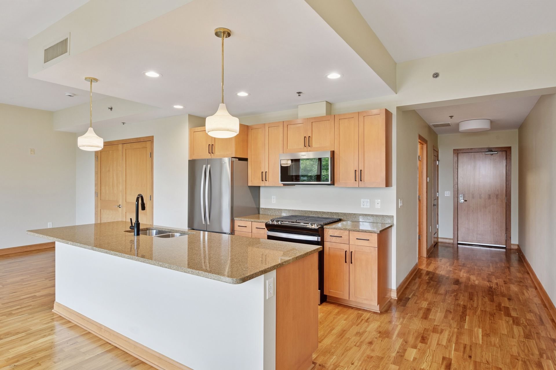 Modern kitchen with wooden cabinets, granite countertops, stainless steel refrigerator and microwave, hardwood floors, and two pendant lights above the island.