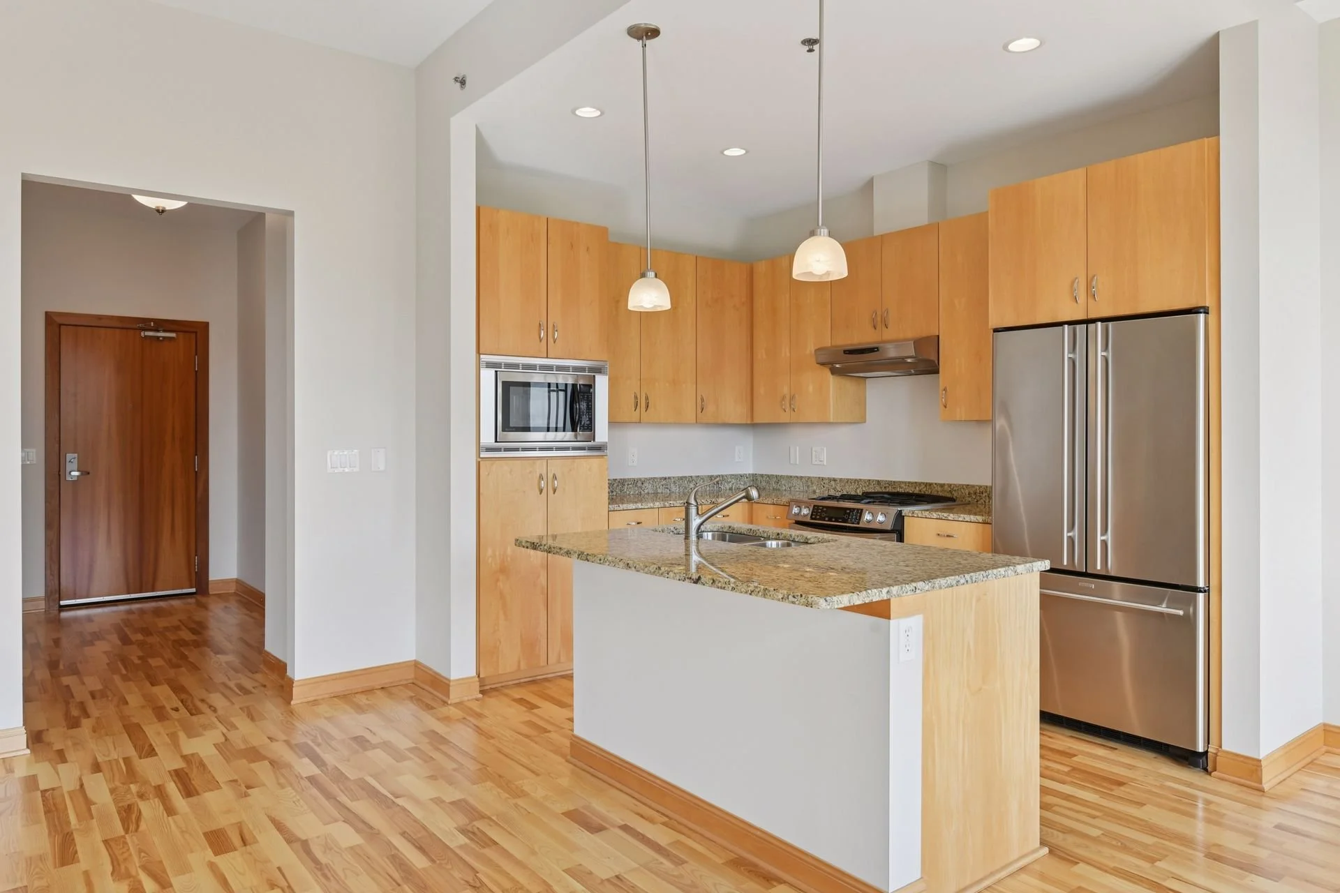 Modern kitchen with wood cabinets, granite countertops, stainless steel appliances, and hardwood floors. There are two hanging pendant lights over the kitchen island.