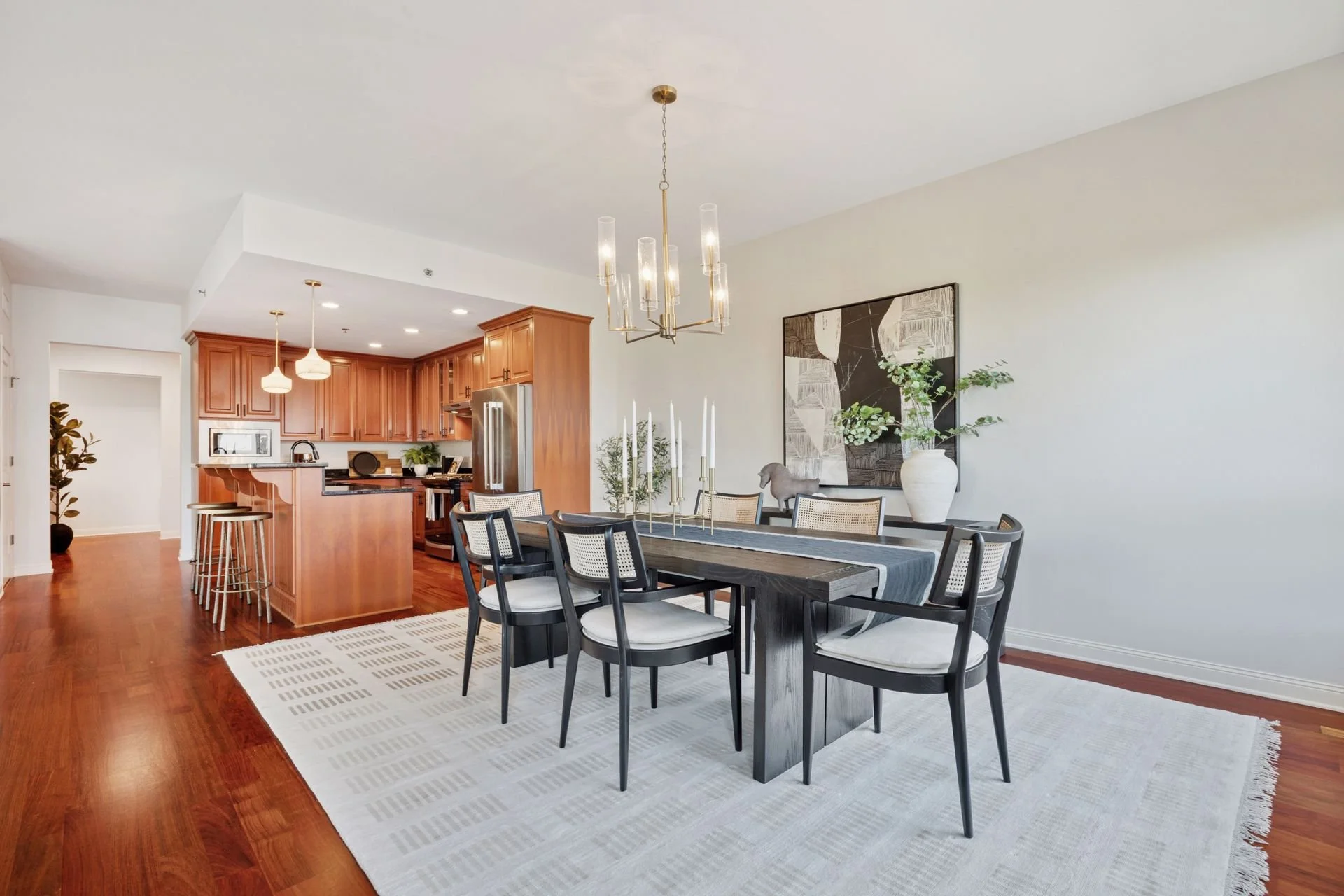 Dining area in front of open kitchen with wooden cabinets, stainless steel appliances, and pendant lighting.