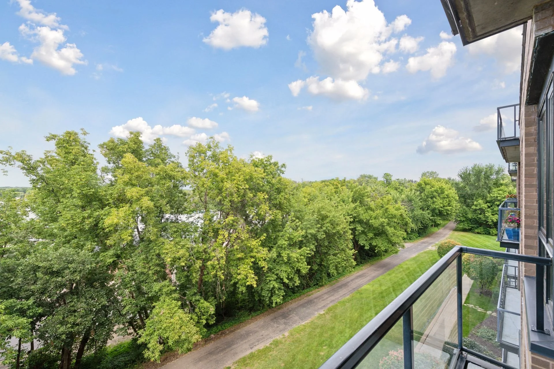 View from a balcony showing green trees and a gravel pathway under a partly cloudy sky.