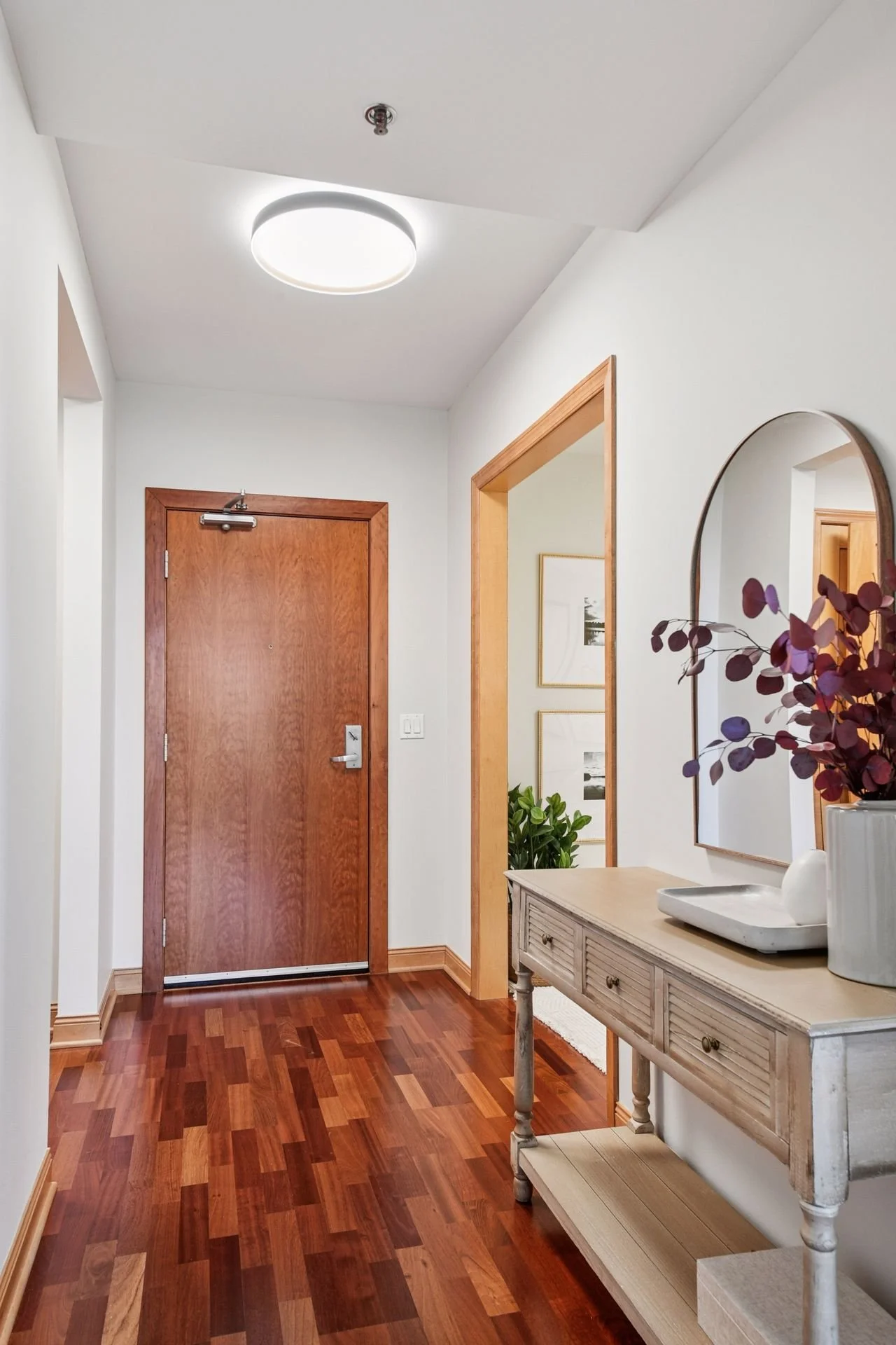 A bright entrance hallway with a wooden front door, and hardwood flooring.