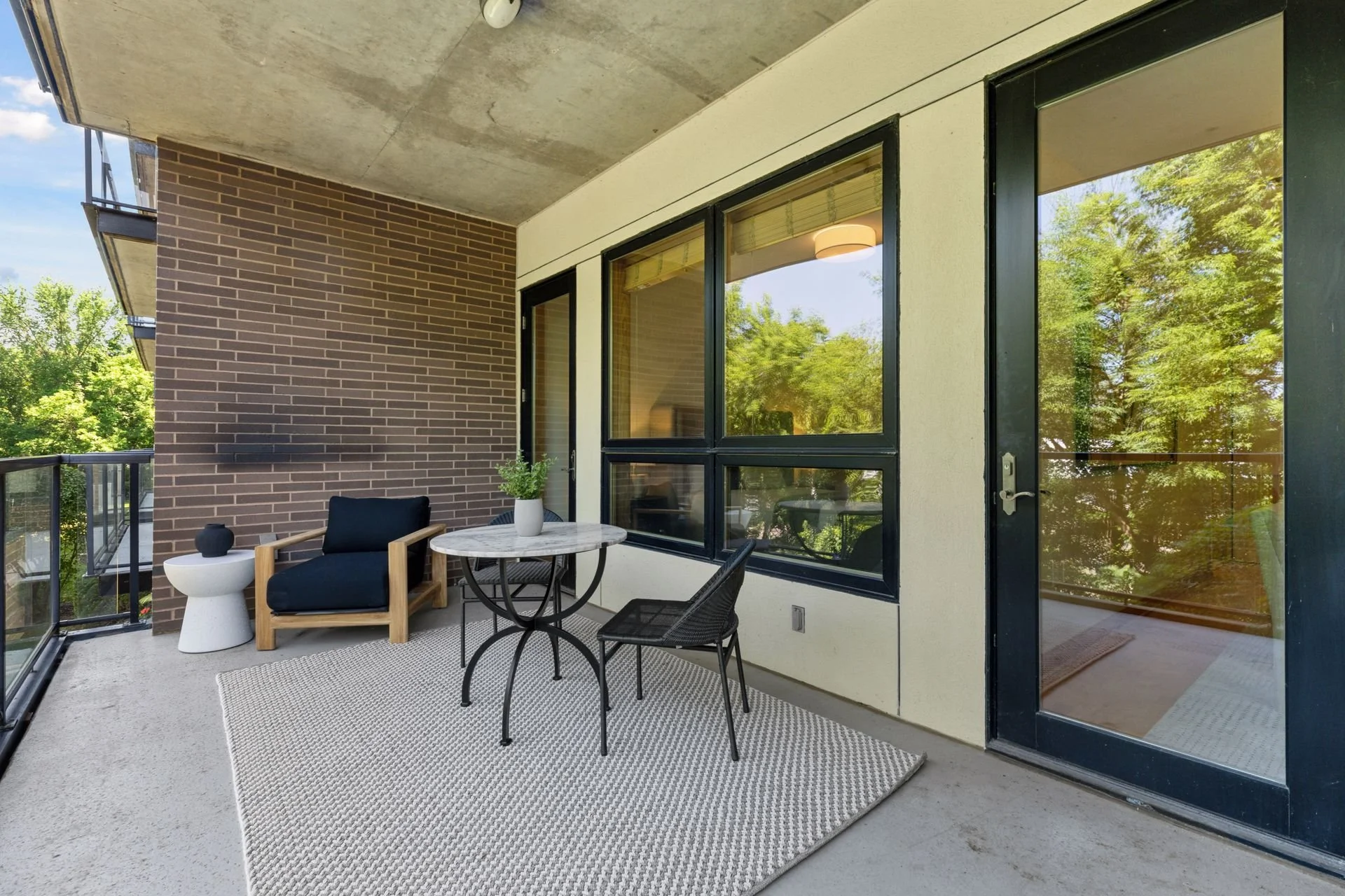 Balcony with large windows, sliding glass door, glass railing, green trees outside, beige carpet, and partial ceiling view.