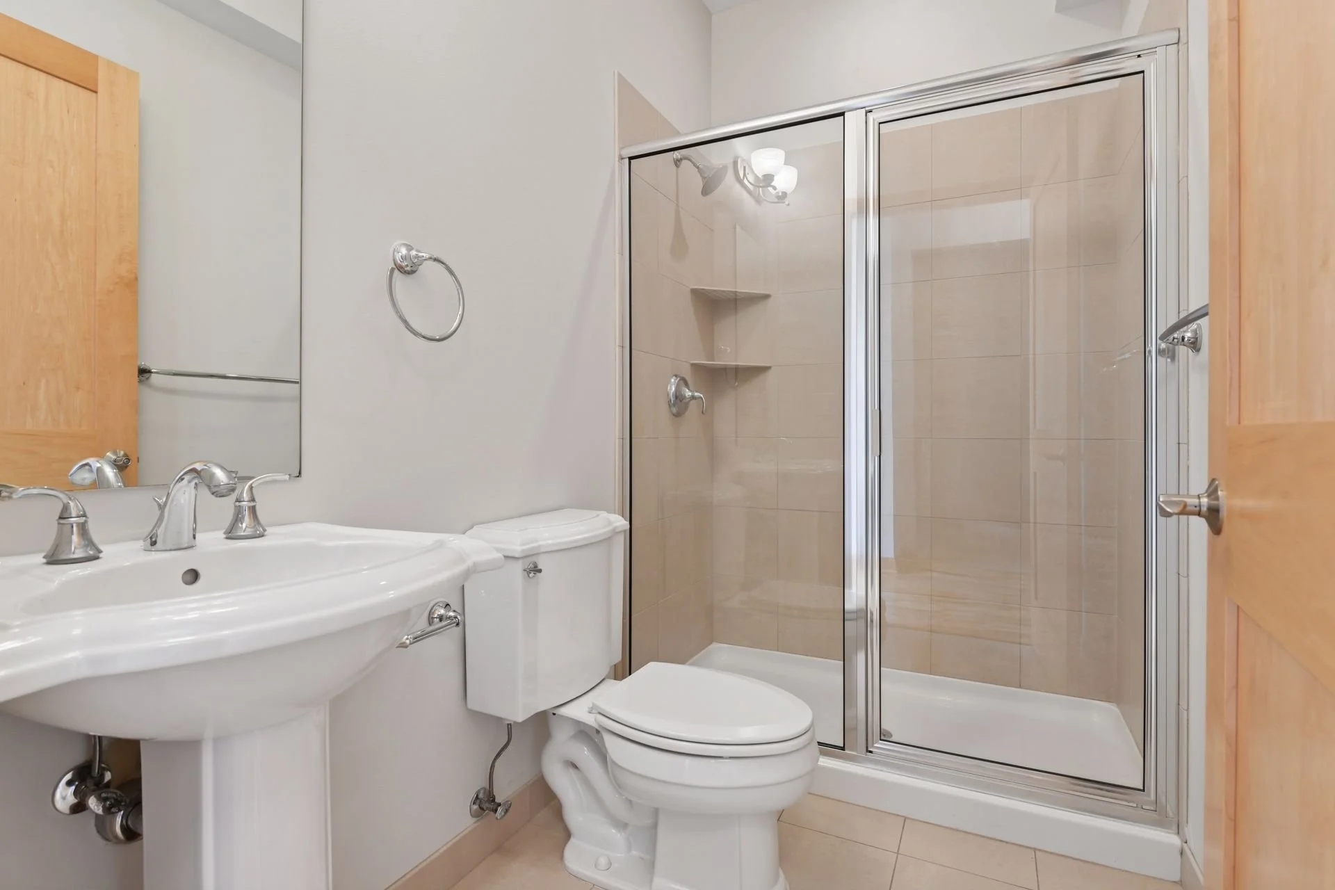 Small bathroom with a white sink, a toilet, a mirrored cabinet, and a glass shower enclosure with beige tiles.