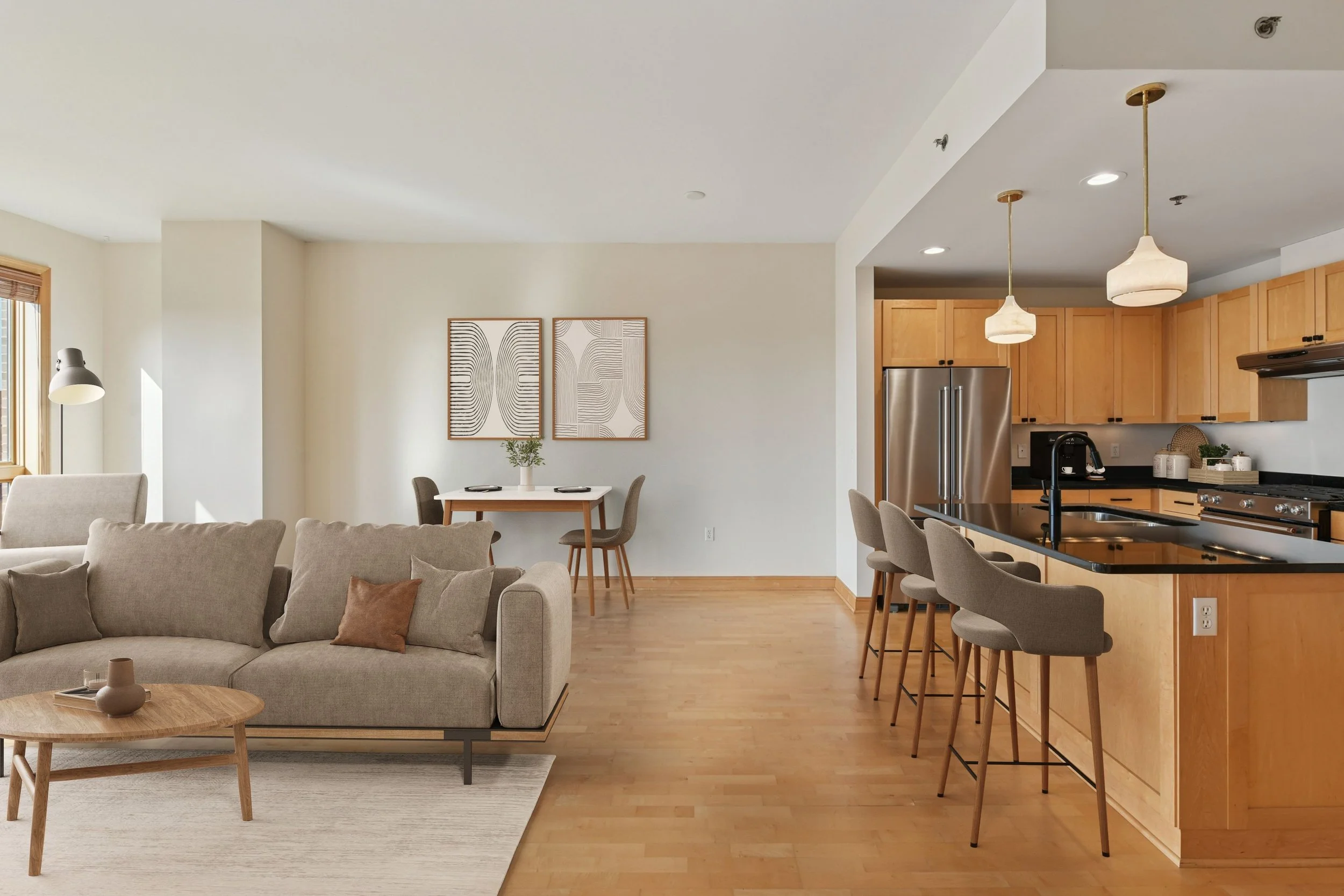 Open-concept living room and kitchen with beige sofa, small wooden coffee table, dining table with chairs, kitchen island with barstools, hardwood floors, and modern decor.