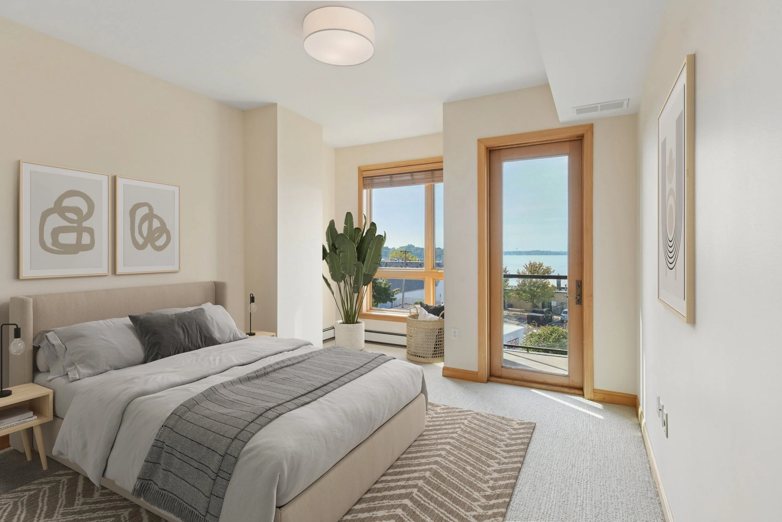 A bedroom with a large bed, white bedding, and three abstract art pieces on the wall above the headboard. There is a large window and a glass door leading to a balcony, with a view of water and trees outside. The room has beige walls, a beige carpet,