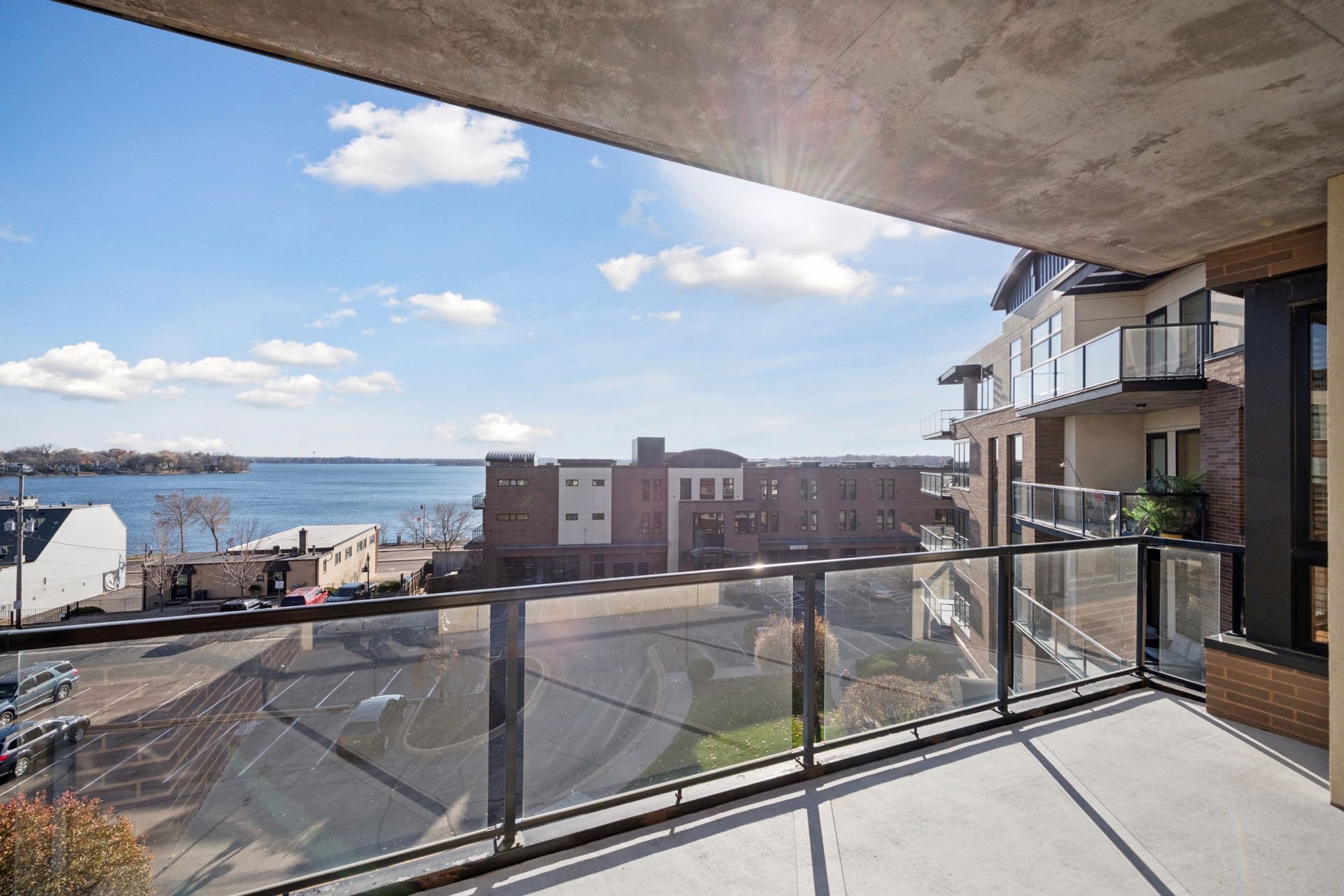 View from a balcony overlooking a parking lot, buildings, Lake Minnetonka, and a sky with clouds.