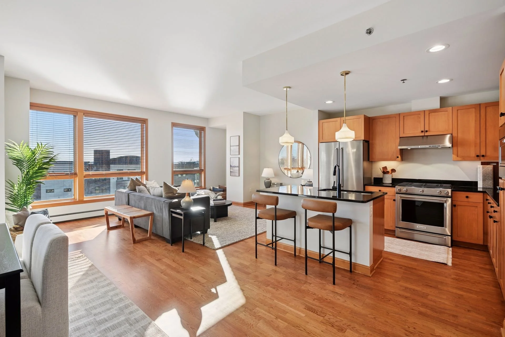 Open-concept living room and kitchen with large windows, hardwood floors, pendant lights, and stainless steel appliances.