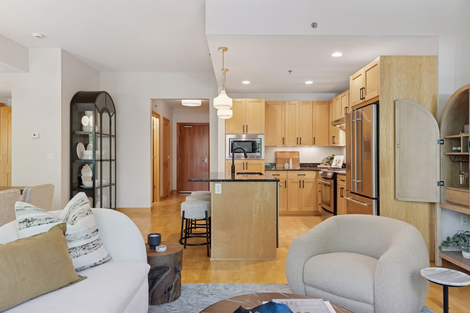 Open-concept living room and kitchen with light wood cabinets, granite countertops, and stainless steel appliances.
