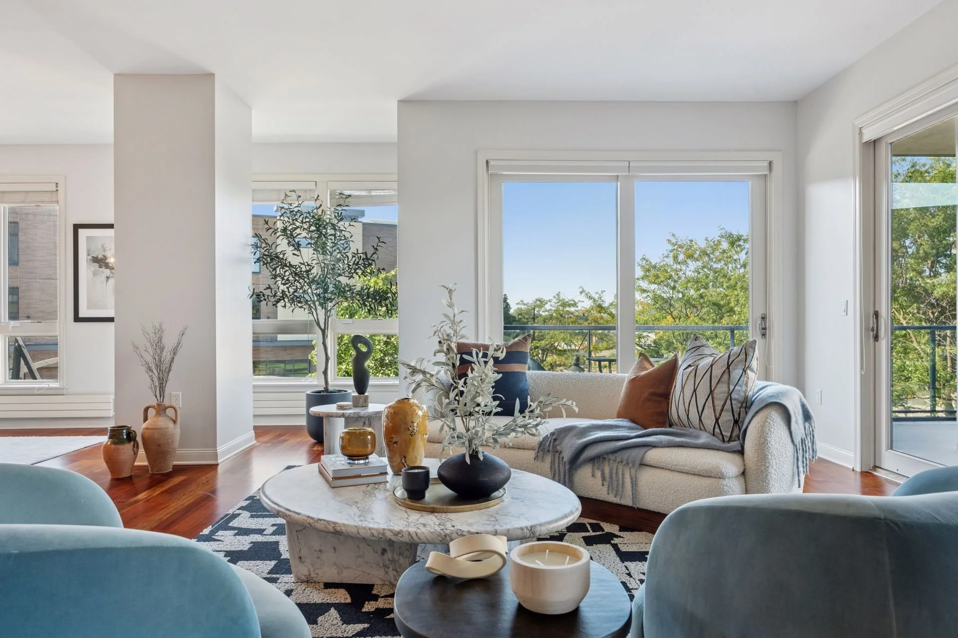 Modern living room with white walls, large windows, and a view of trees outside.