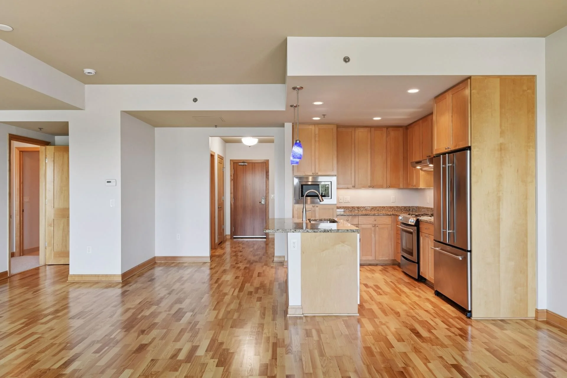 Modern condo interior with hardwood floors, open living space, and a kitchen with light wooden cabinets and stainless steel appliances.