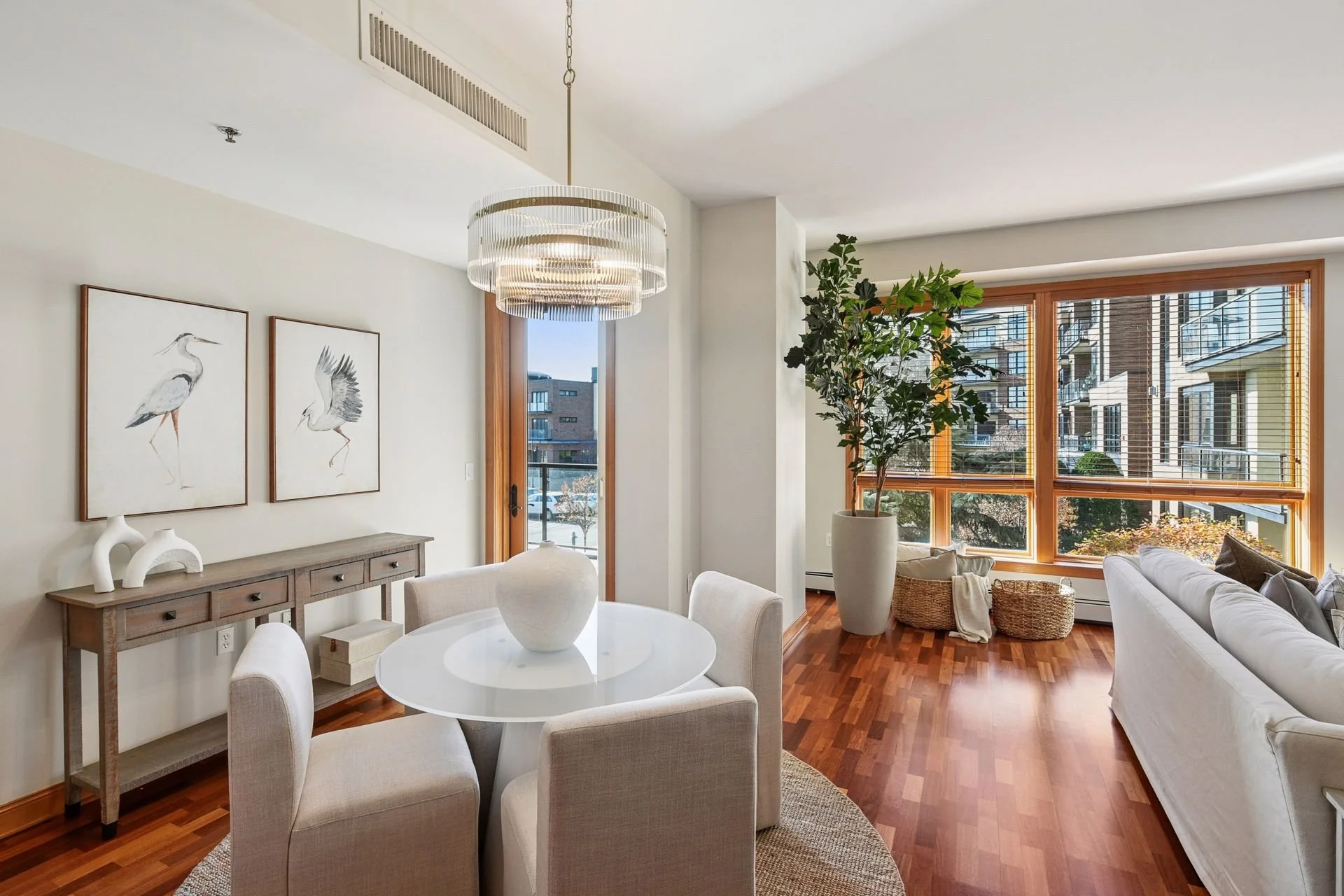 Spacious living room with white walls, hardwood floors, and large windows with wooden blinds.