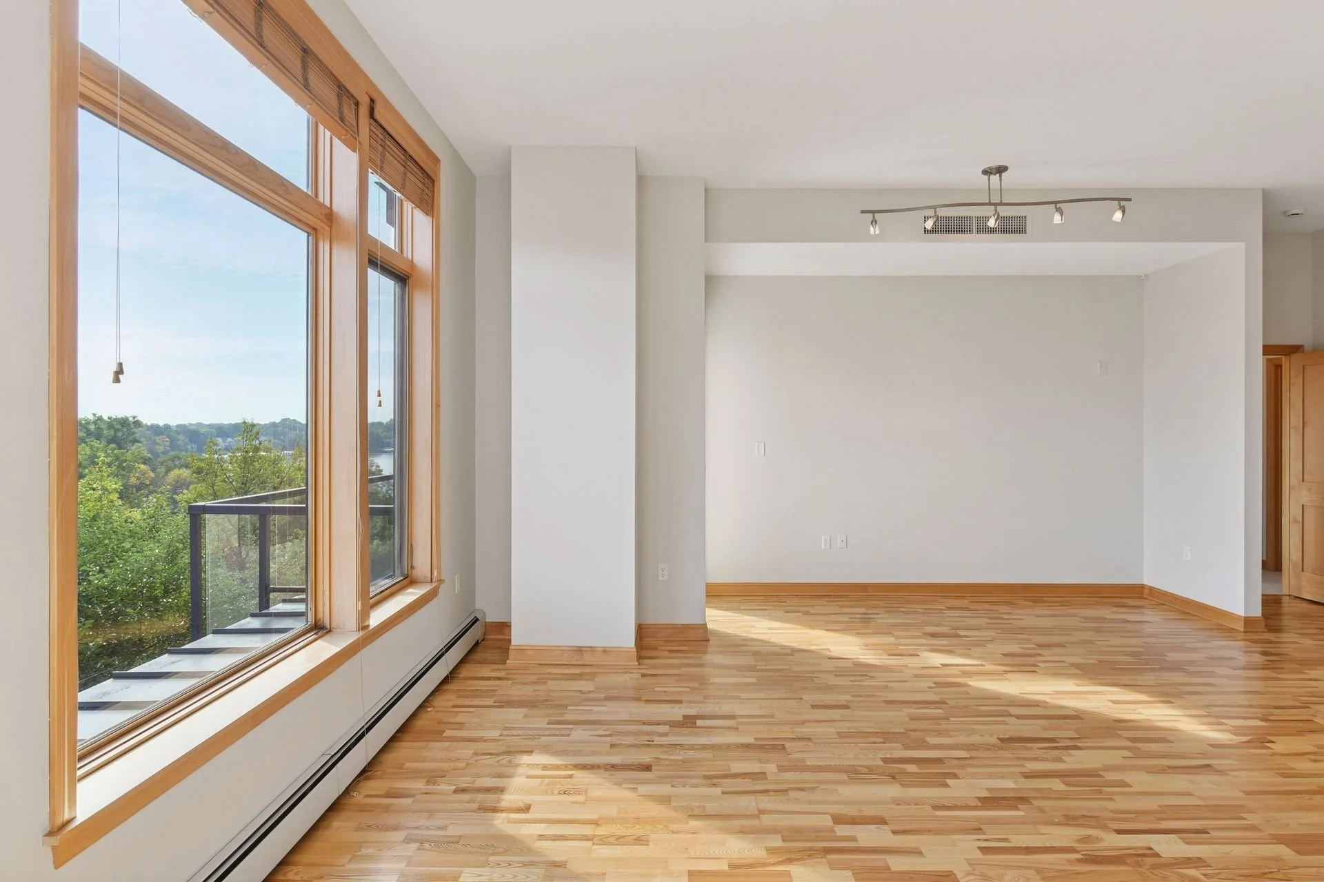 Empty living room with large window, hardwood floor, white walls, and wooden trim.