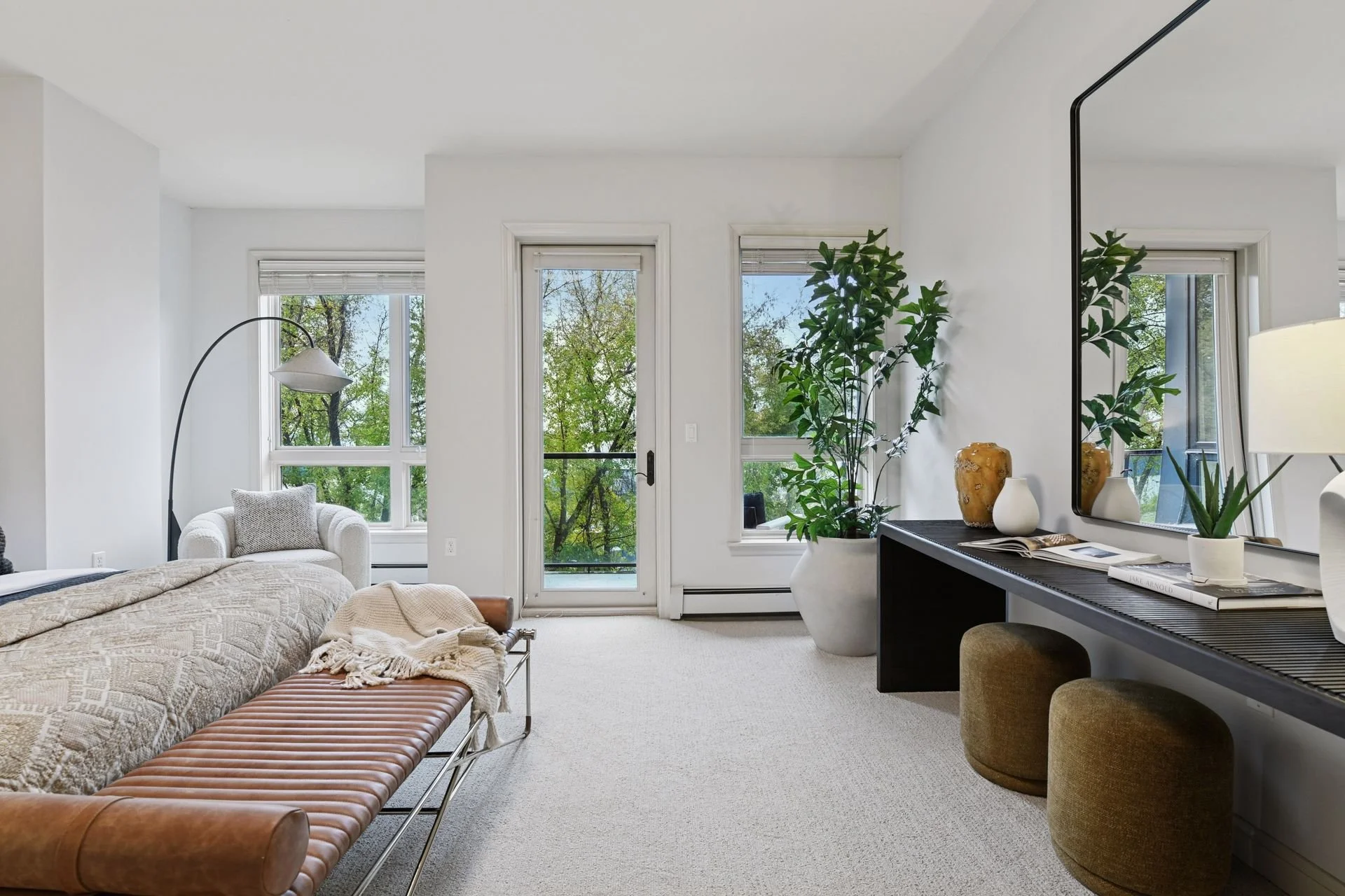 Bright living room with large windows, a door leading to a balcony and green trees visible outside.