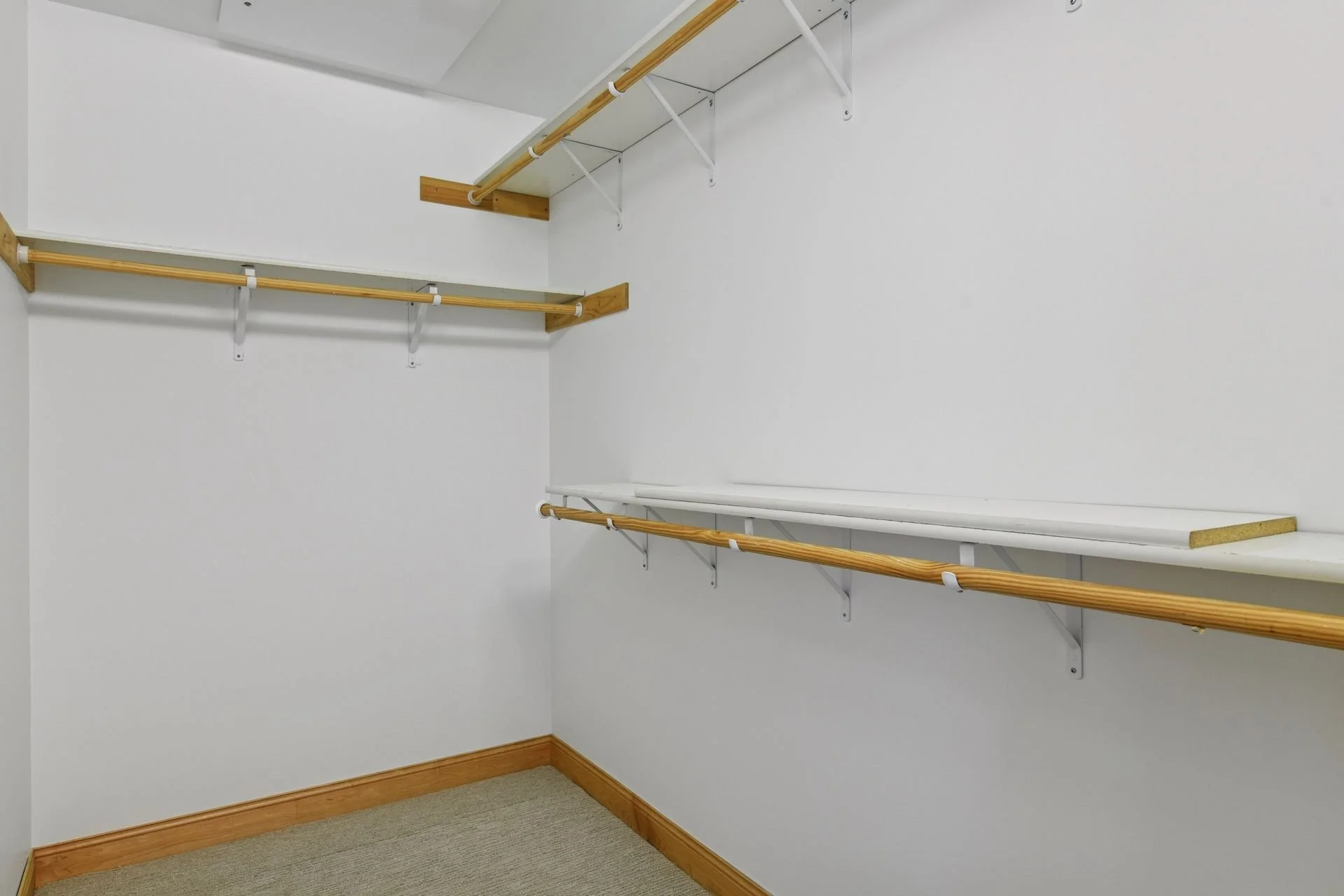 Walk-in closet with white walls, wooden trim, and multiple wooden and white shelves with hanging rods.