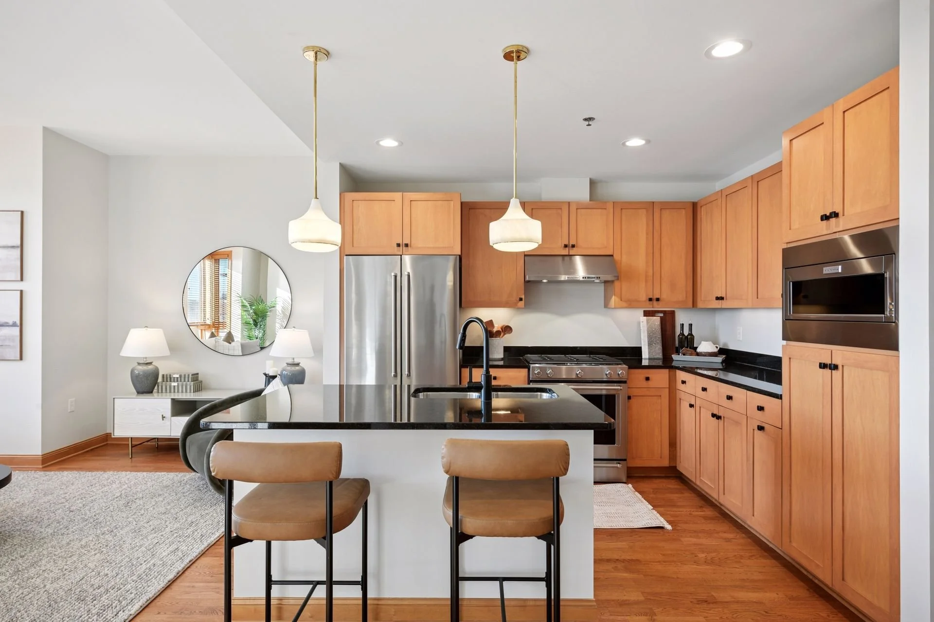 Modern kitchen with wooden cabinets, stainless steel refrigerator, black countertops, and pendant lights over a spacious island.