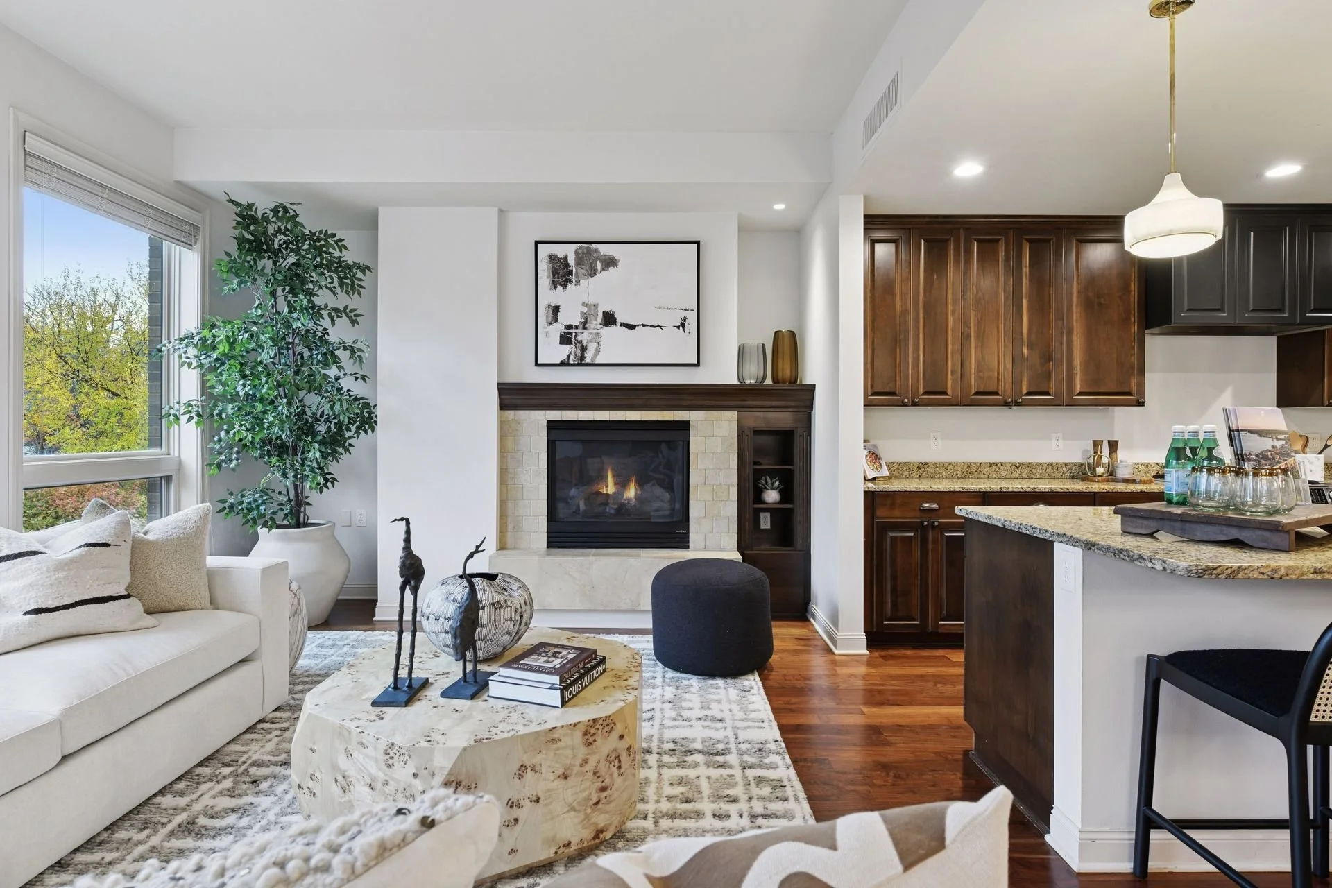 Living room with a fireplace with wooden mantel, granite countertop kitchen with dark wood cabinets, and hardwood floors.