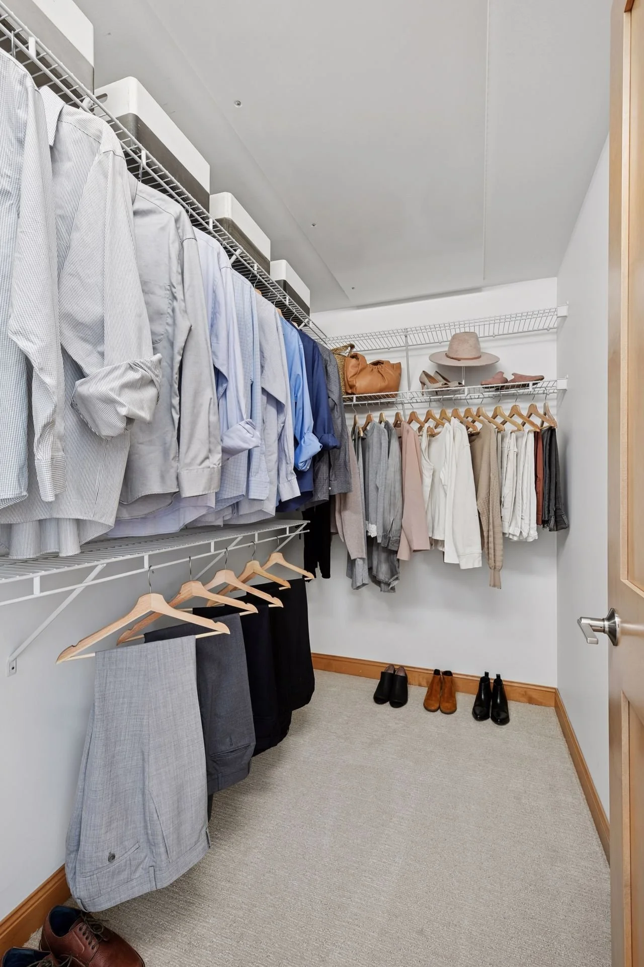 A walk-in closet with wire shelves, beige carpet, white walls, and light wood trim.