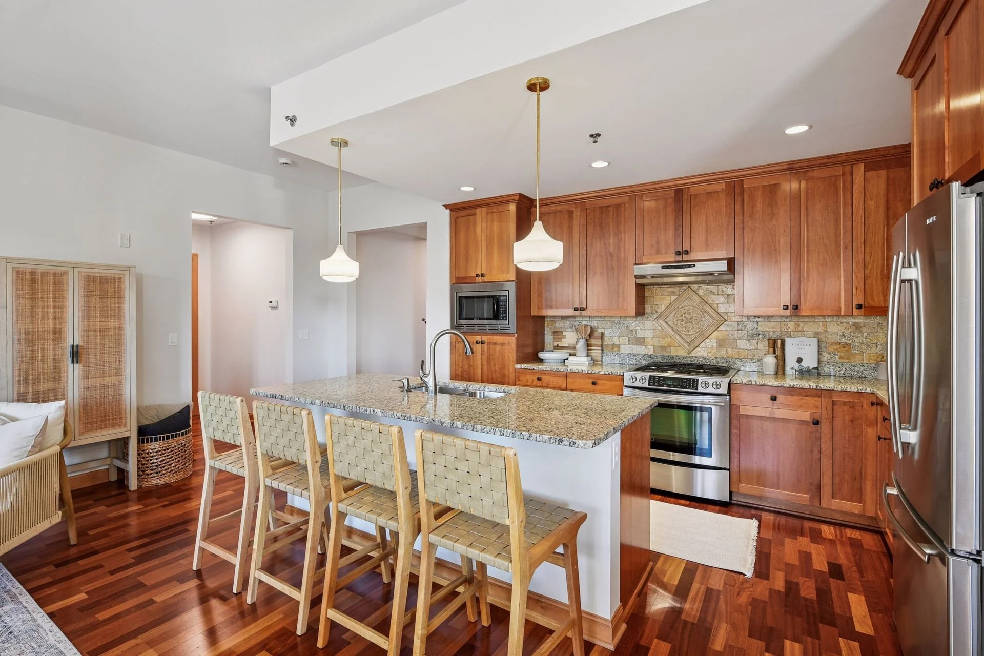 Modern kitchen with wooden cabinets, granite countertop island, stainless steel appliances, and two hanging pendant lights.