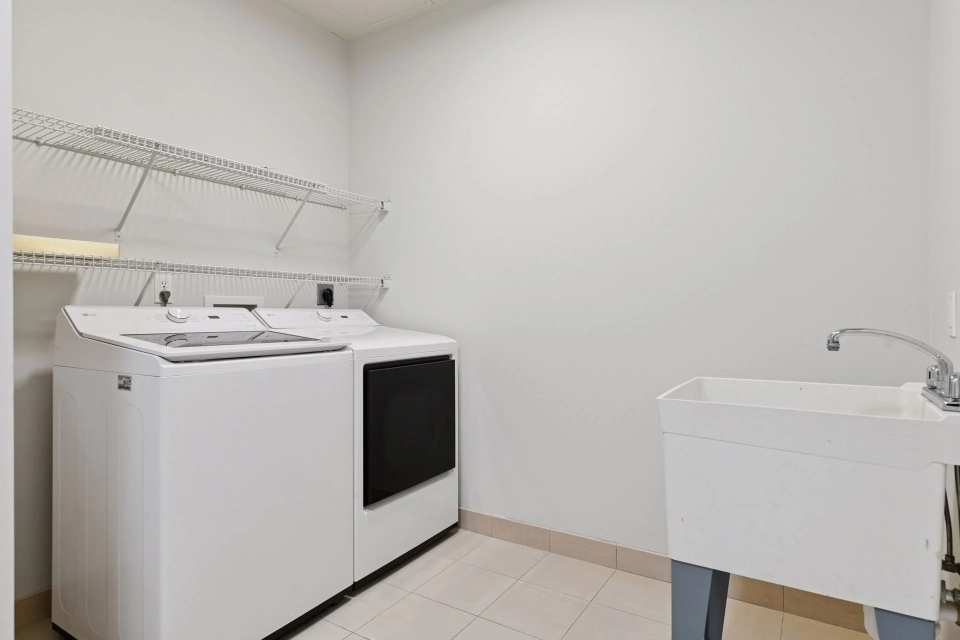 Laundry room with white washing machine and dryer, white wire shelves above, and a utility sink on the right side.