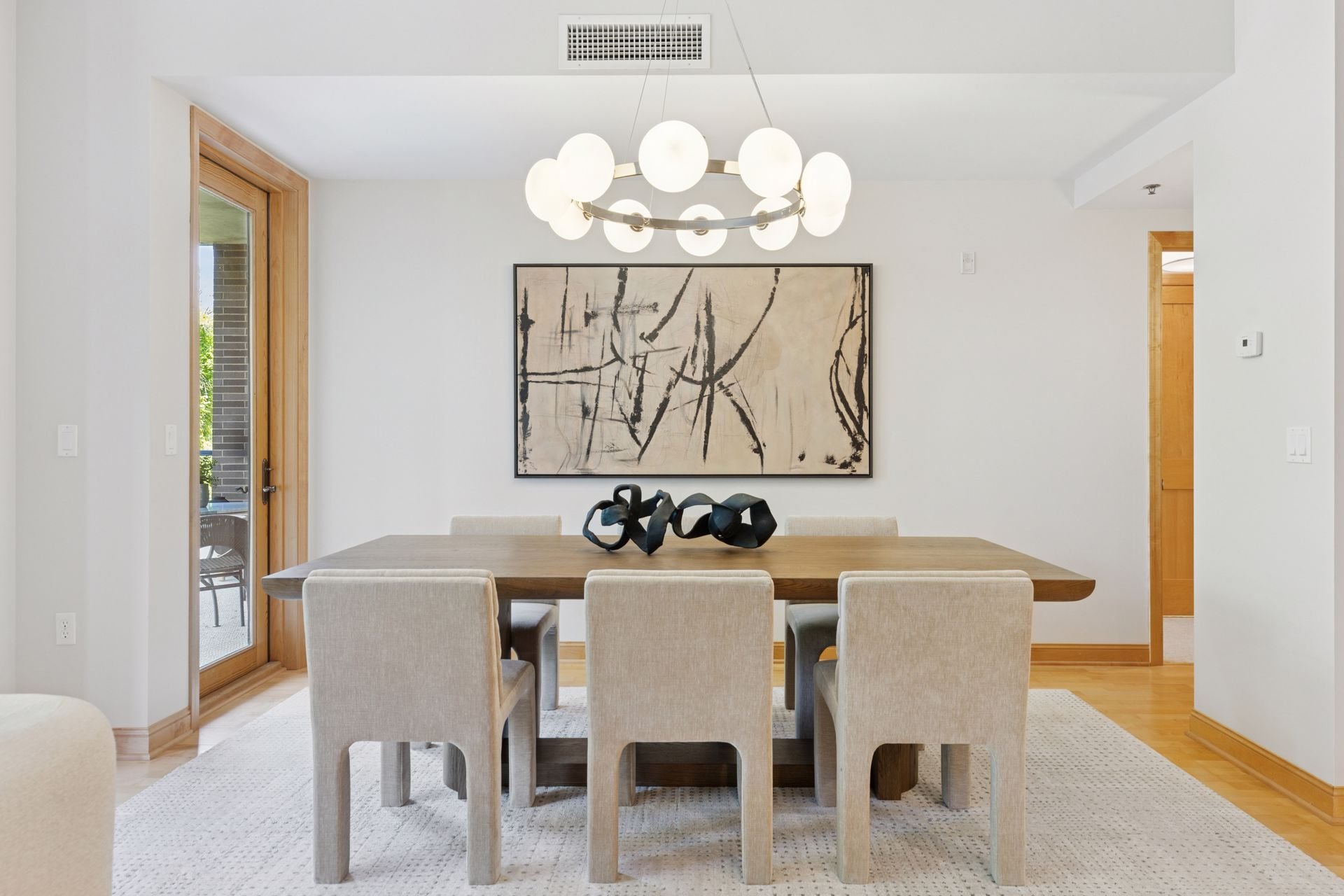 Modern dining room with white walls, a contemporary chandelier, and a glass door leading outside.