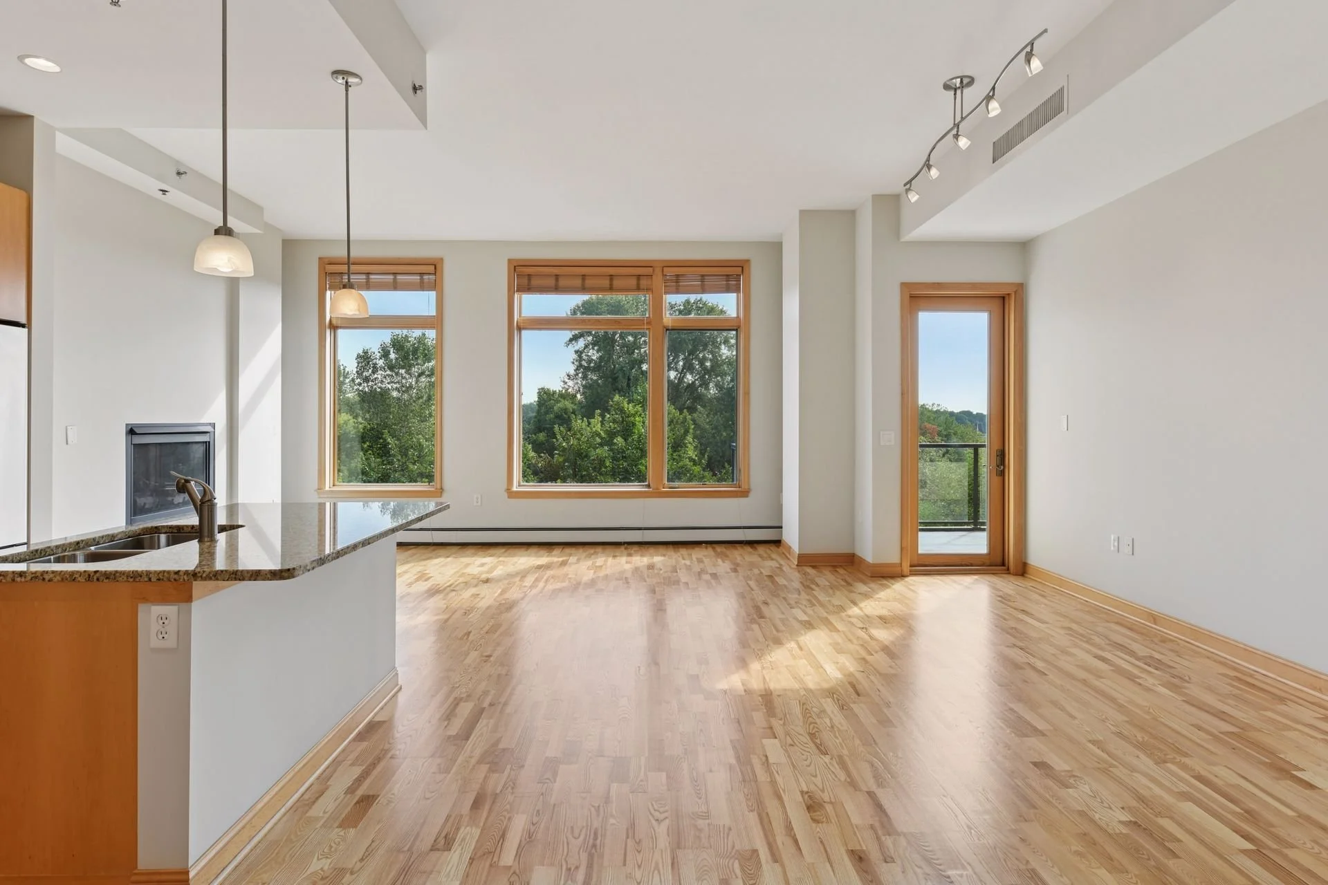 Empty living area with large windows, hardwood flooring, and a sliding glass door leading to a balcony.