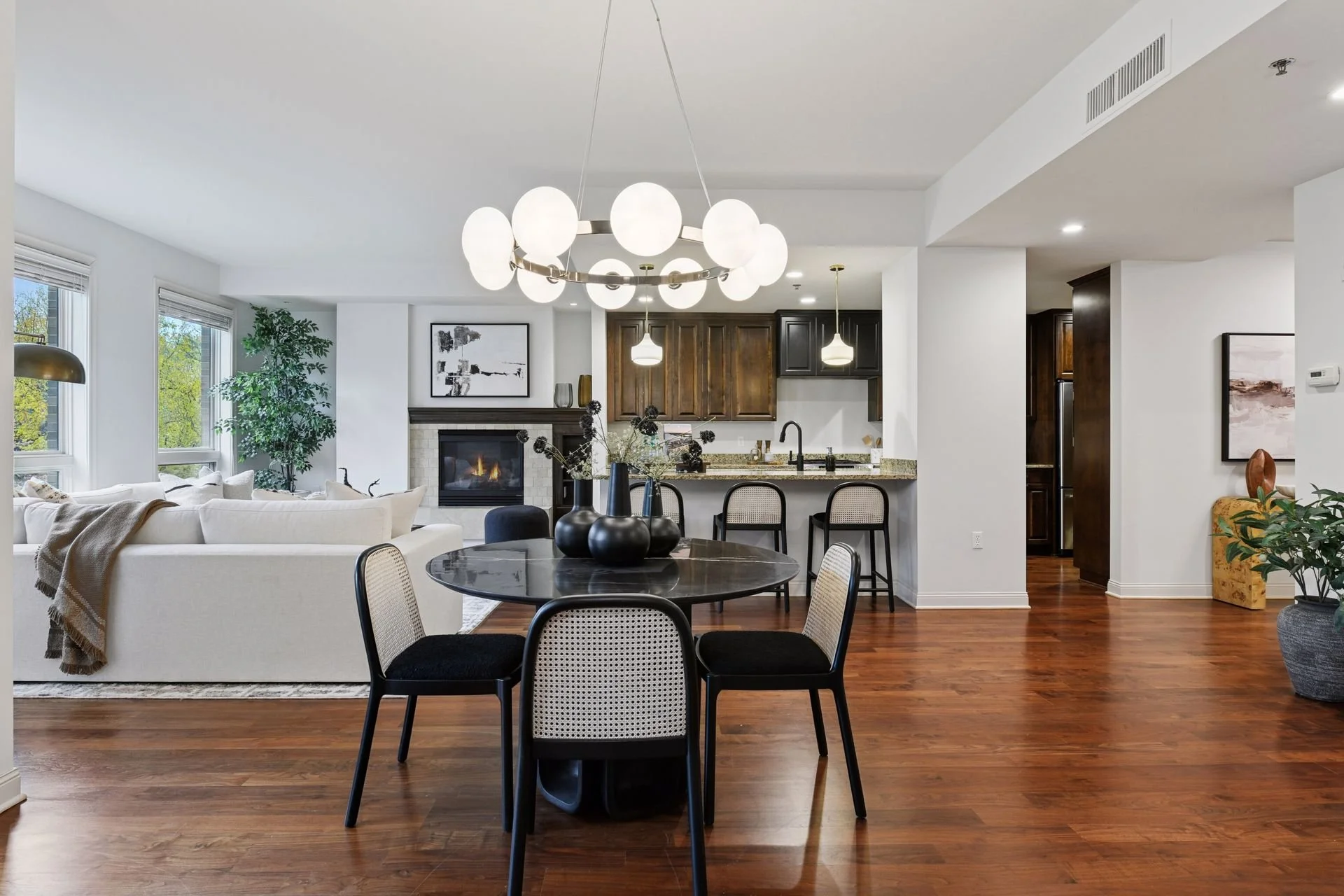 Living and dining room with a fireplace, windows, a kitchen with dark cabinets, and a granite countertop.