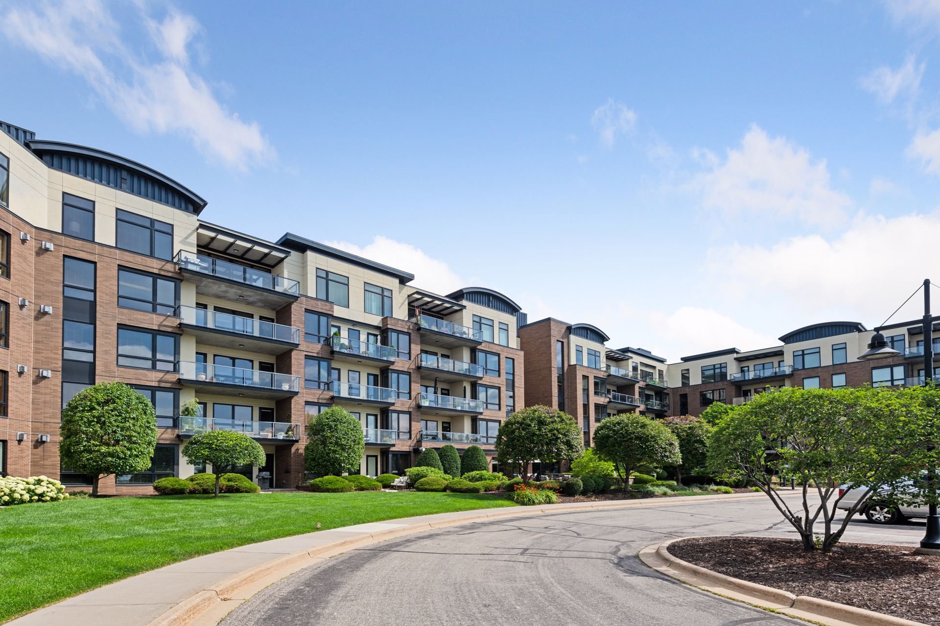 Modern multi-story apartment building with balconies, surrounded by well-maintained green lawns and trees, under a blue sky in Spring Park, MN.