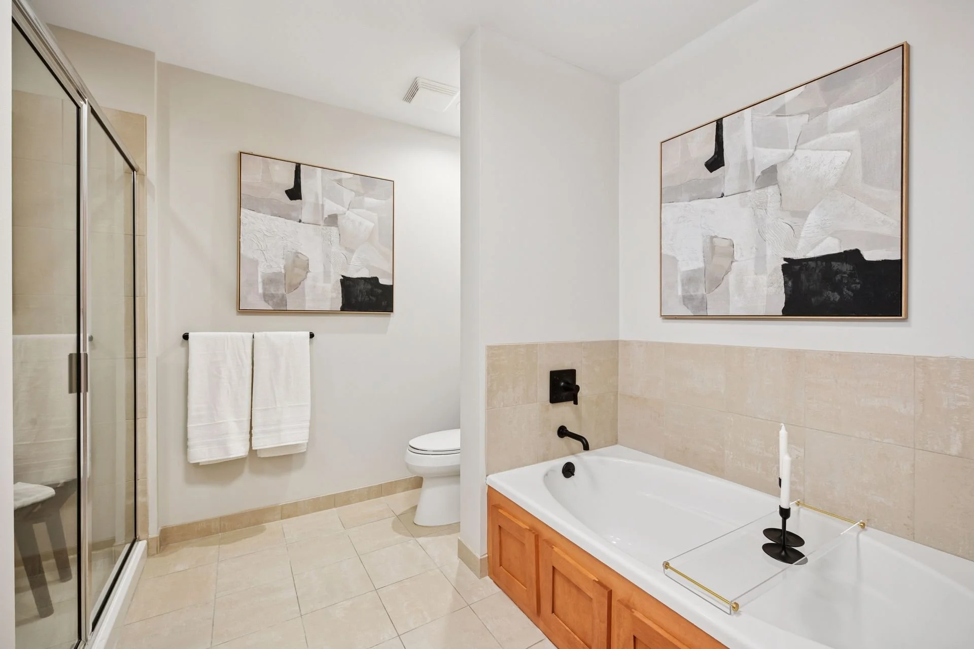 Modern bathroom with a glass shower, a toilet, a bathtub with a wooden panel, and beige tiled flooring.