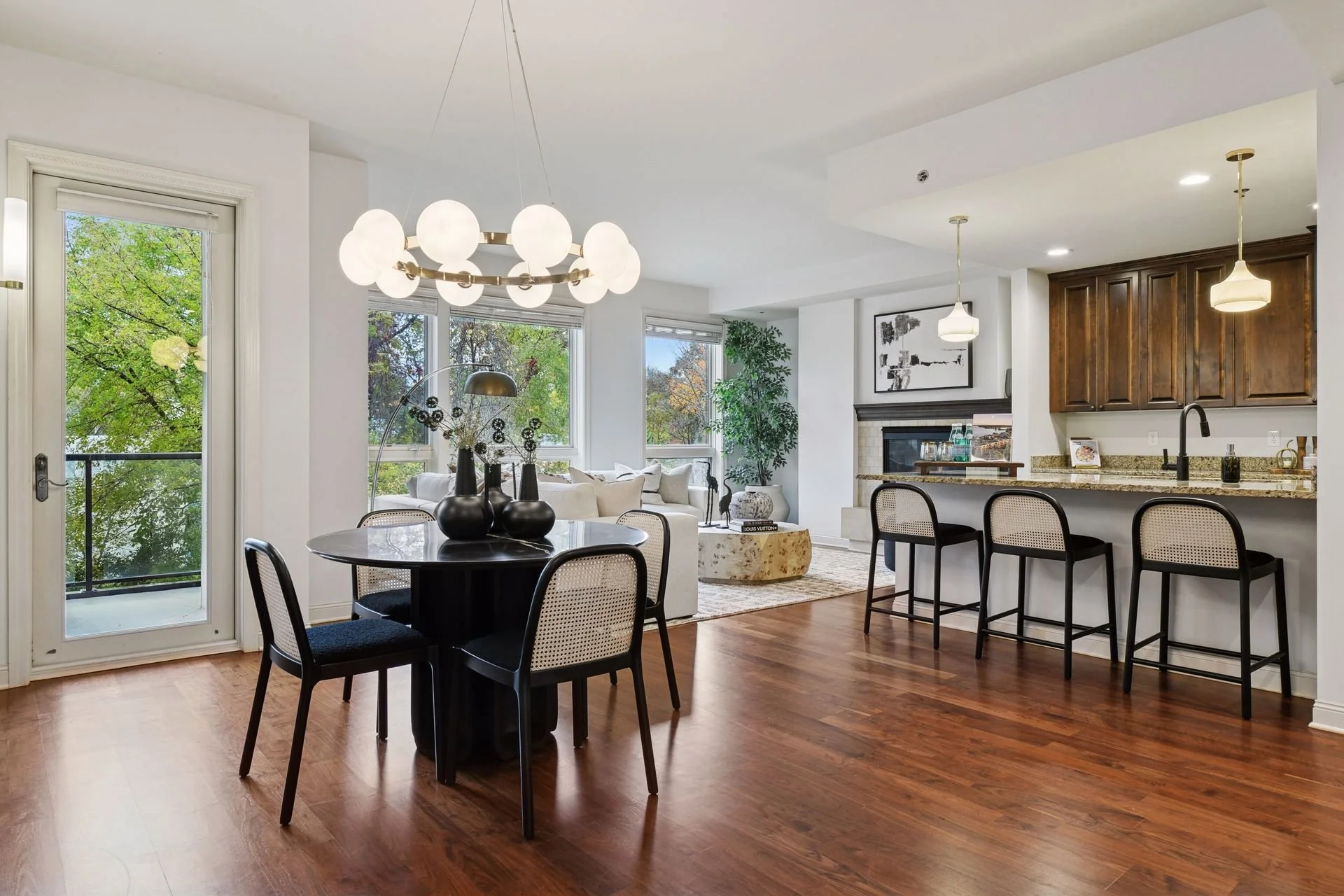 Open-concept living and dining area with hardwood floors and kitchen with dark wooden cabinets and a granite countertop.