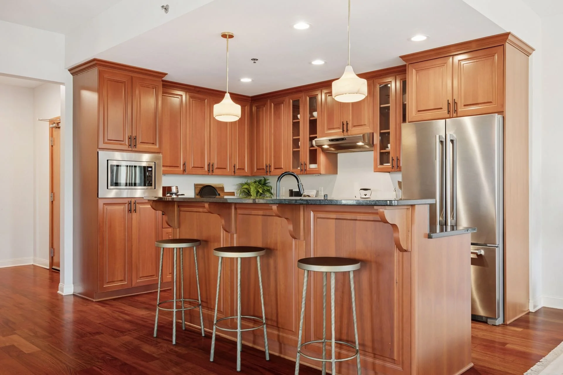 Kitchen with wooden cabinets, stainless steel appliances, a black countertop island, and pendant lights.