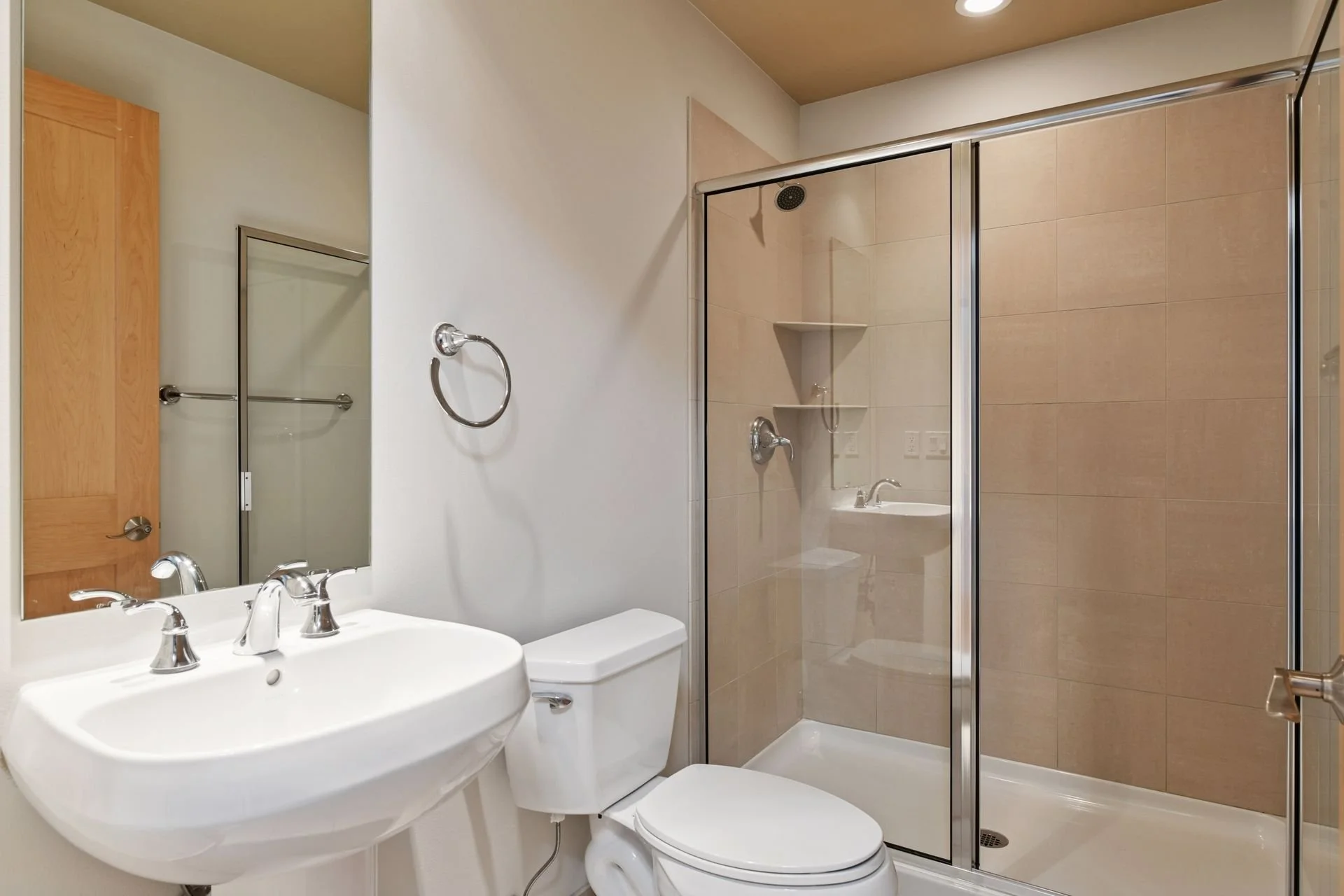 Bathroom with a white sink, mirror, toilet, and a glass enclosed shower with beige tiles.