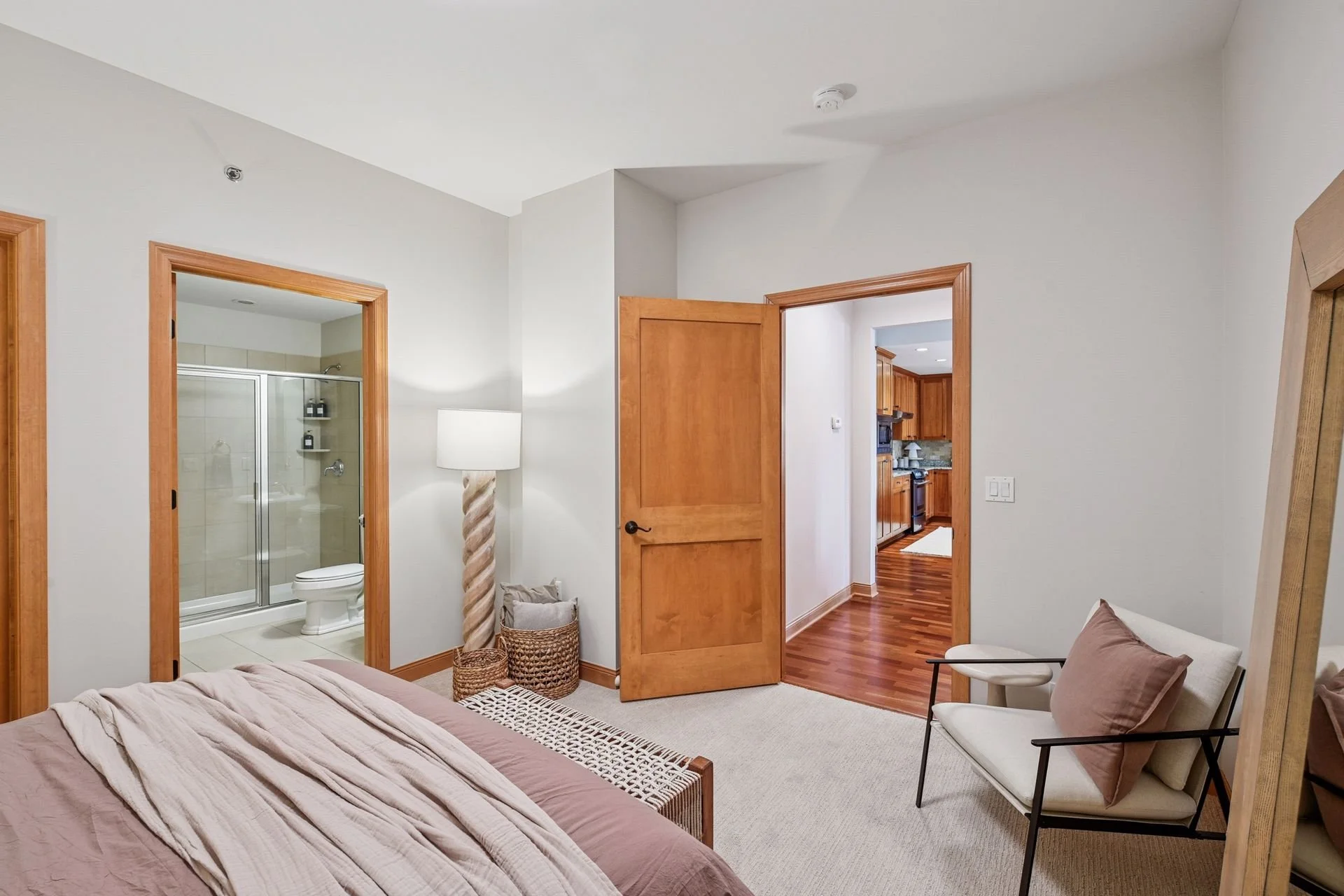 A bedroom and a door leading to a bathroom with a glass shower and toilet, and a door to a hallway with wooden flooring.