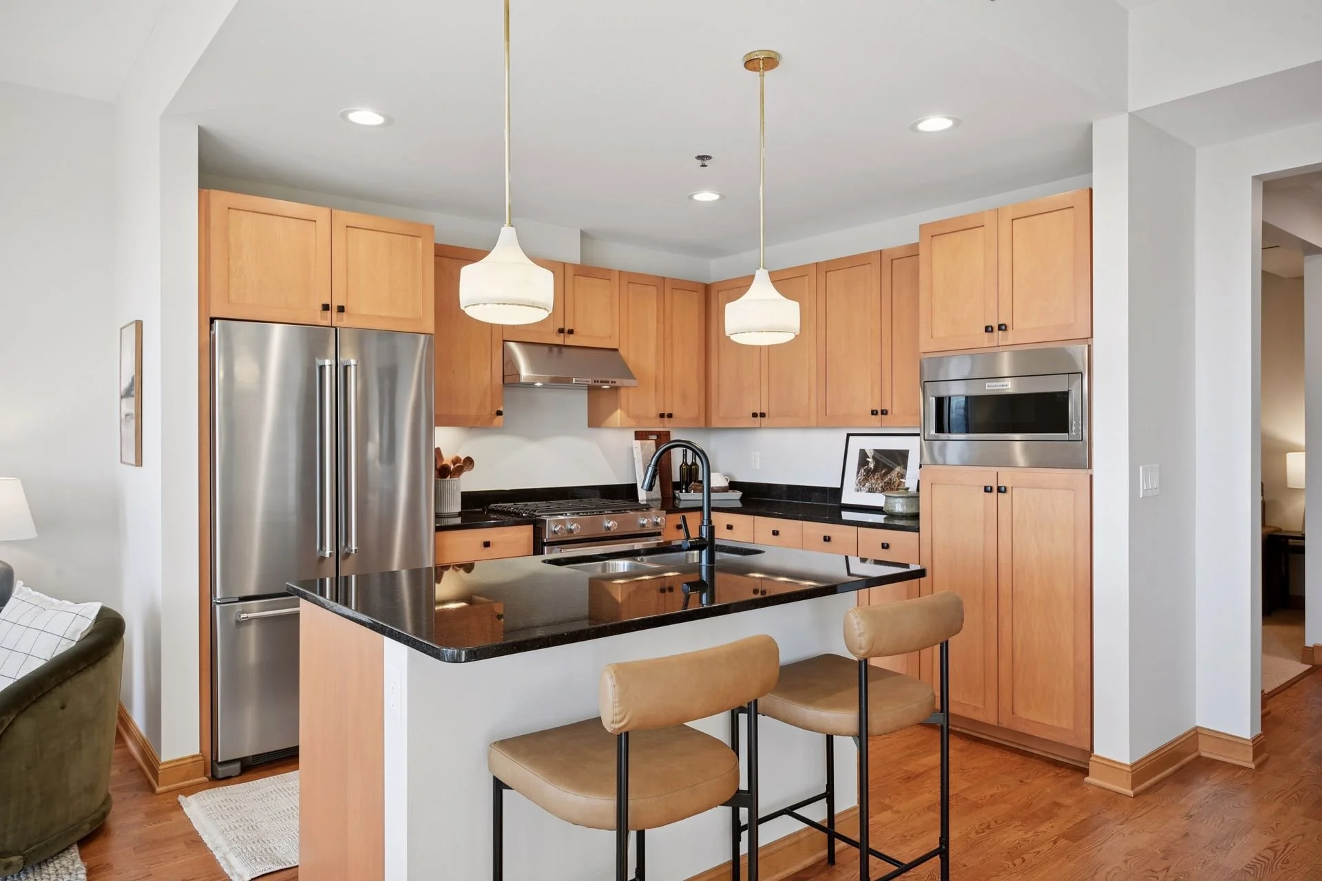 Modern kitchen with wooden cabinets, black granite countertops, stainless steel refrigerator, oven, microwave, and a kitchen island.