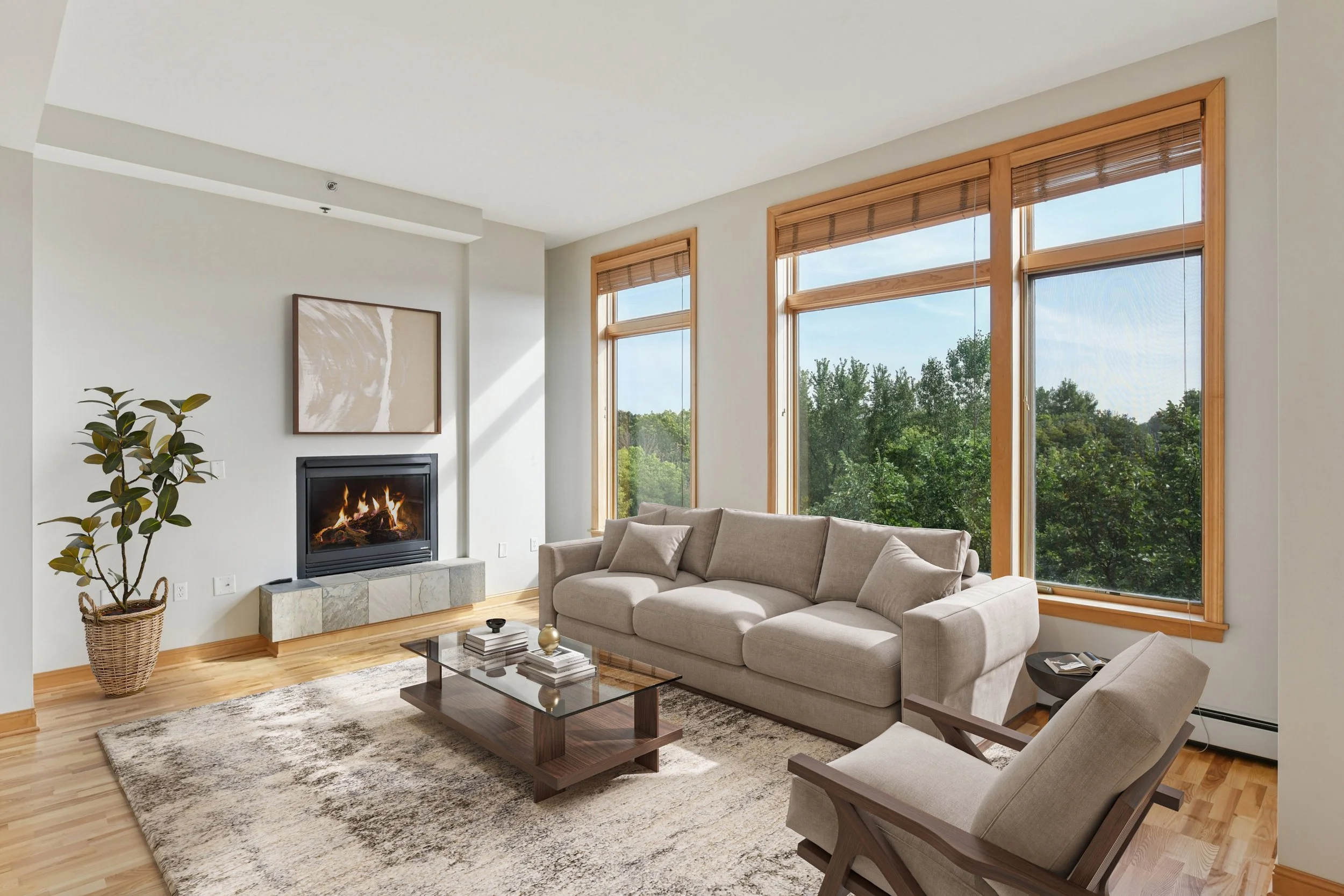 Modern living room with a beige sofa, wooden armchair, glass coffee table, fireplace, large windows with wooden frames, a potted plant, and a rug.
