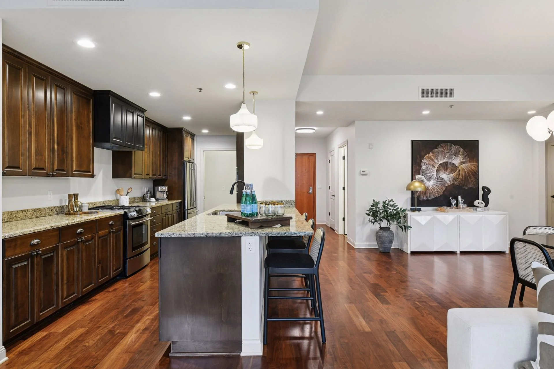Open-concept kitchen with dark wood cabinets, granite countertops, island, and nearby living space.