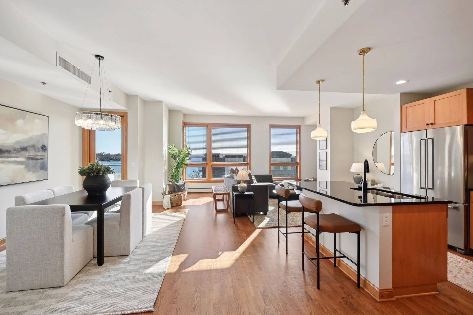 Open-concept living and dining area in a modern apartment with large windows and hardwood floors.
