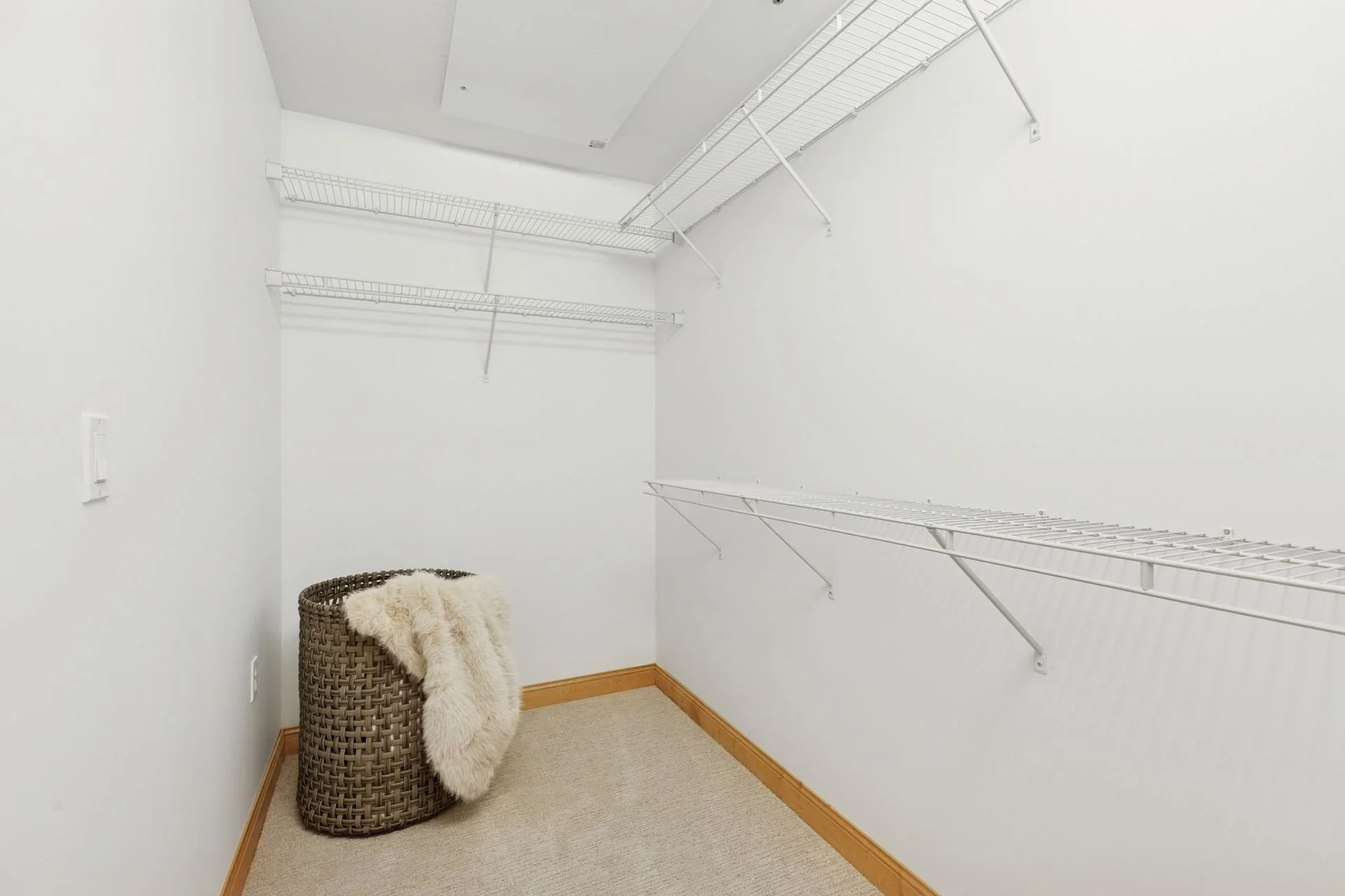 Walk-in closet with white wire shelves on the walls, beige carpeted floor, white walls, and natural wood baseboards.