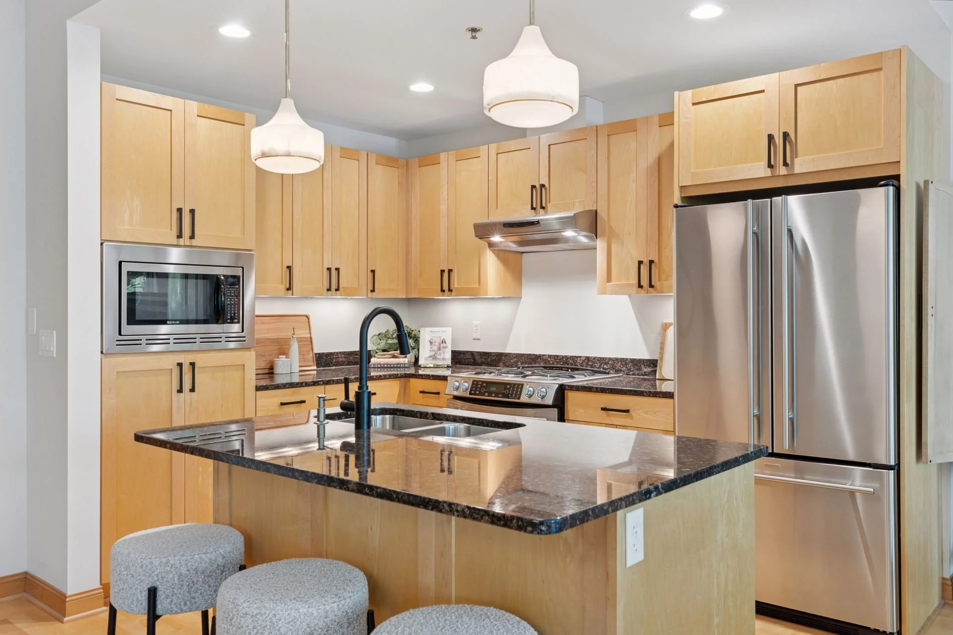 Modern kitchen with wooden cabinets, stainless steel appliances, black granite countertops, and a central island with a black faucet.