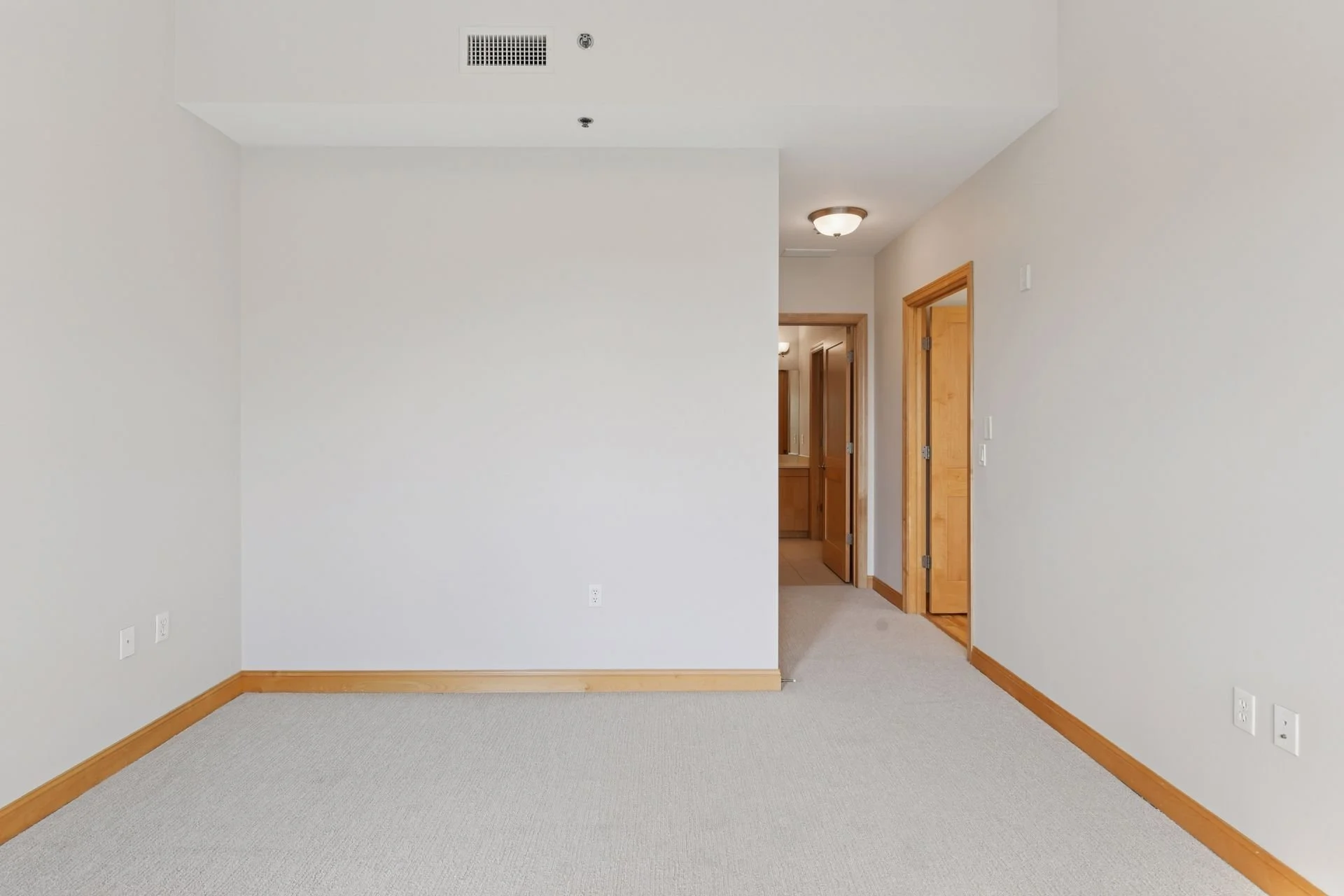 Empty room with beige carpet, white walls, wooden trim, and two doorways leading to other rooms.