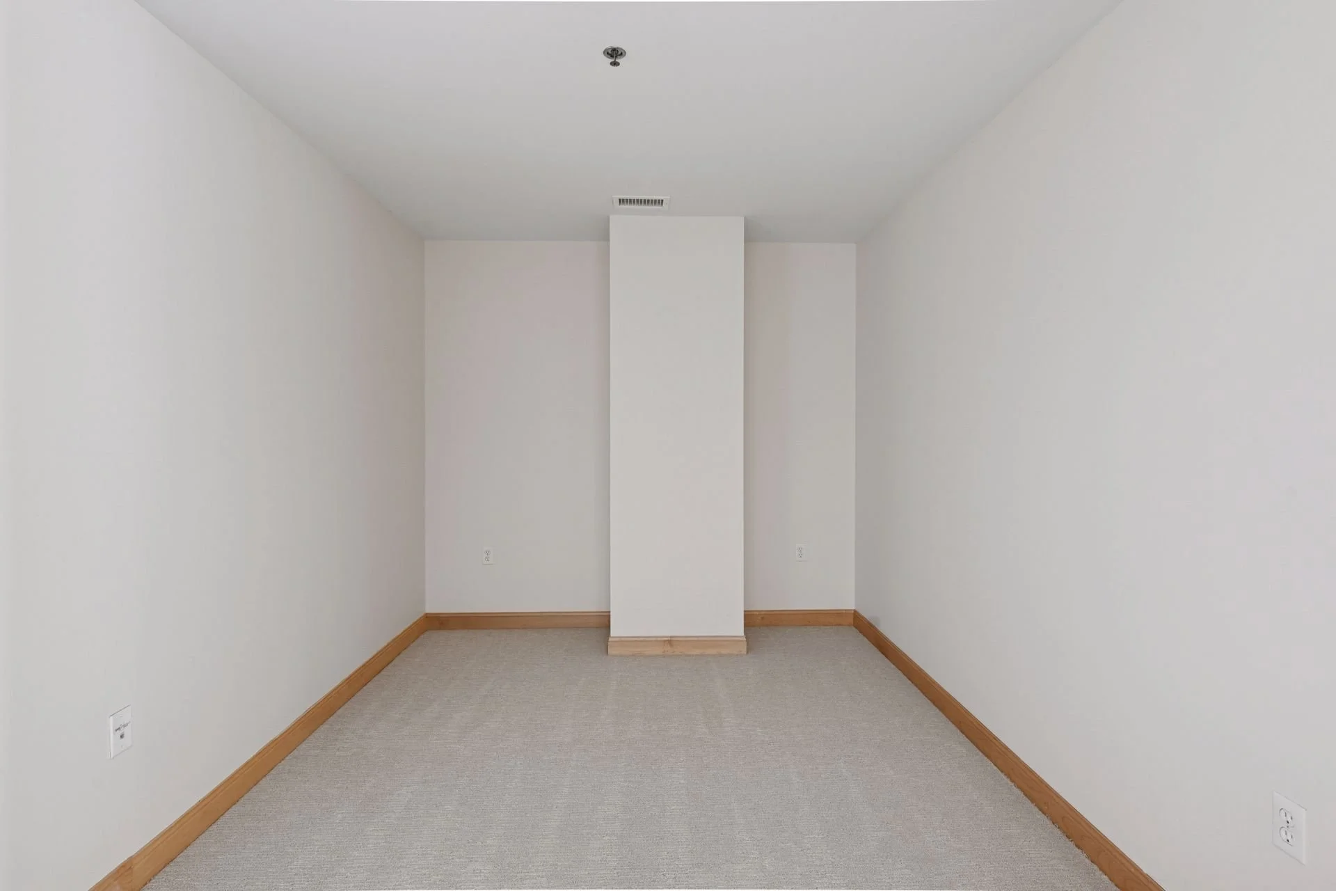 Empty room with beige carpet, white walls, wooden baseboards, and electrical outlets.