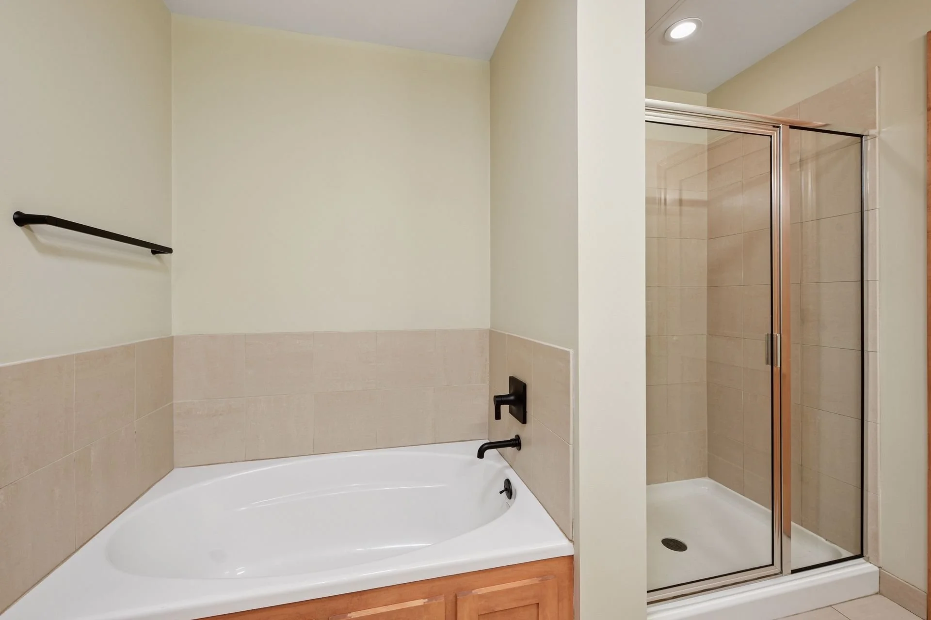 Bathroom with a bathtub, a separate shower enclosure with a glass door, and beige tiled walls.