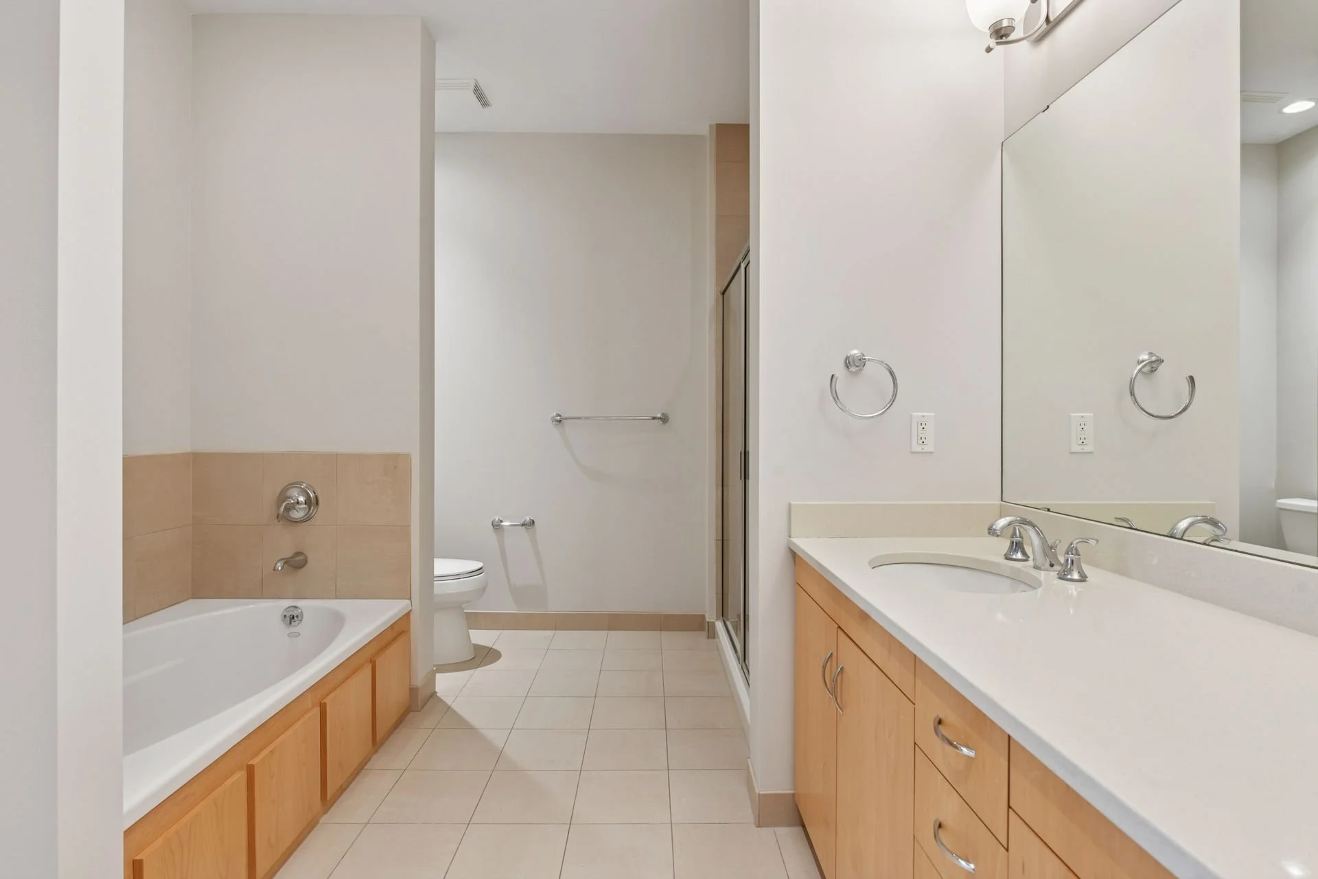 A bathroom with a bathtub, a toilet, a shower enclosure, and a vanity with a sink, large mirror and towel rings.