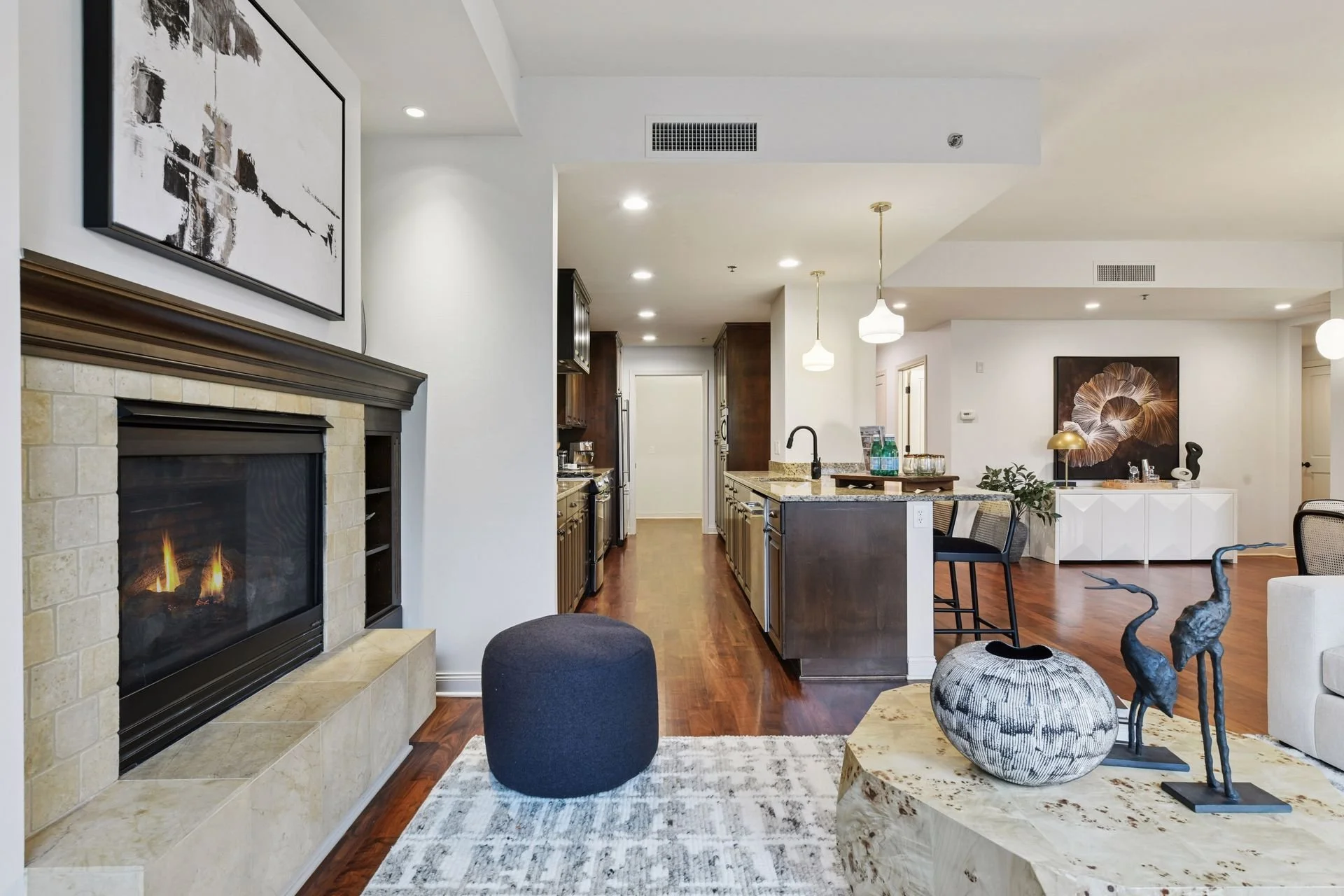 Modern living room with fireplace, wooden flooring, and open kitchen with granite countertops and pendant lights.